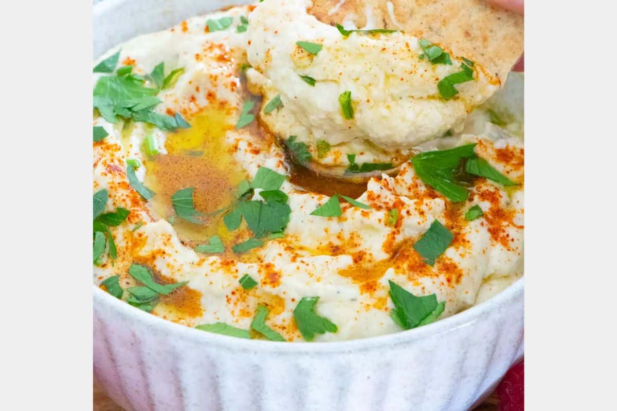 A white bowl with a creamy dip in it and green leaf garnish