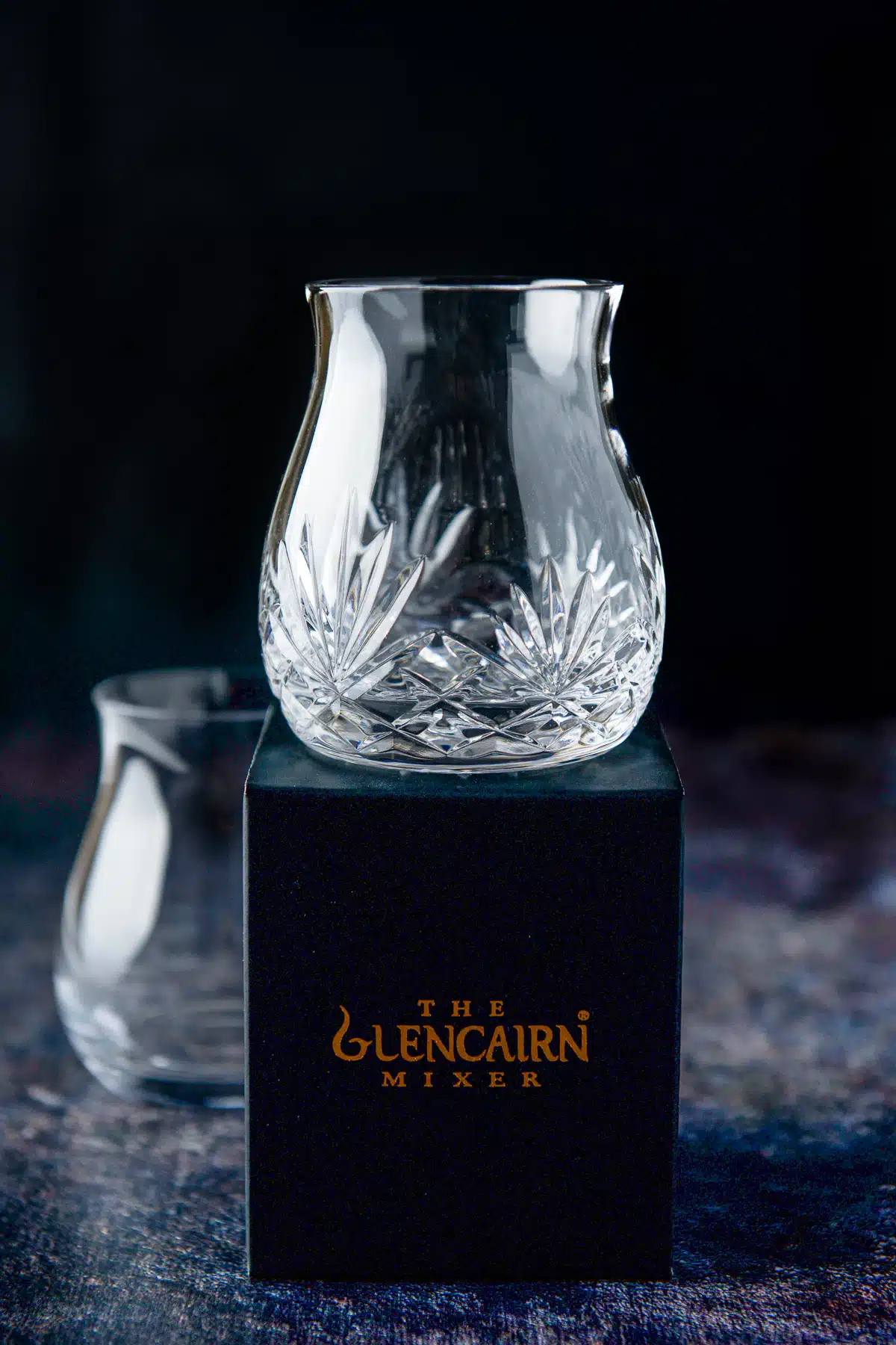 Two Glencairn mixer glasses on a colorful table. One is on top of the box it came in