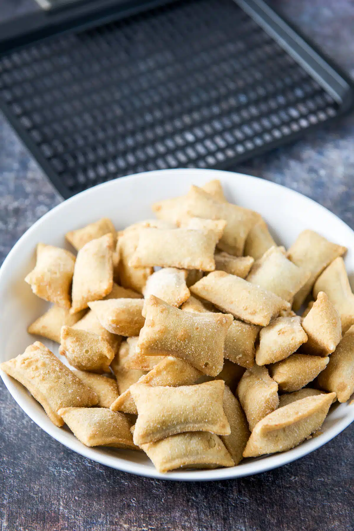 A bowl of frozen pizza rolls and an air fryer tray behind it