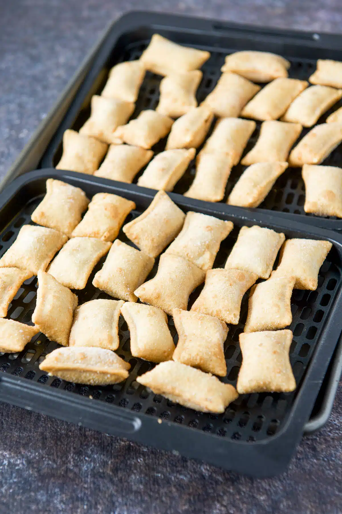 Two air fryer trays covered with frozen pizza rolls