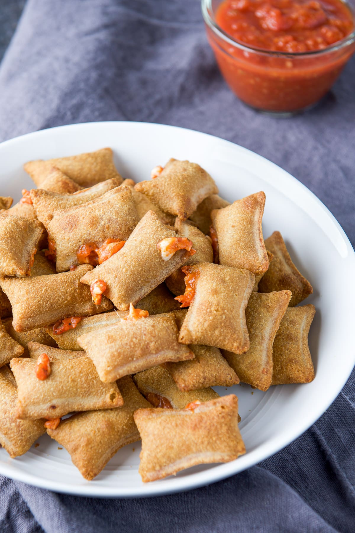 closer view of the pizza rolls oozing cheese and sauce in a bowl with more sauce behind it