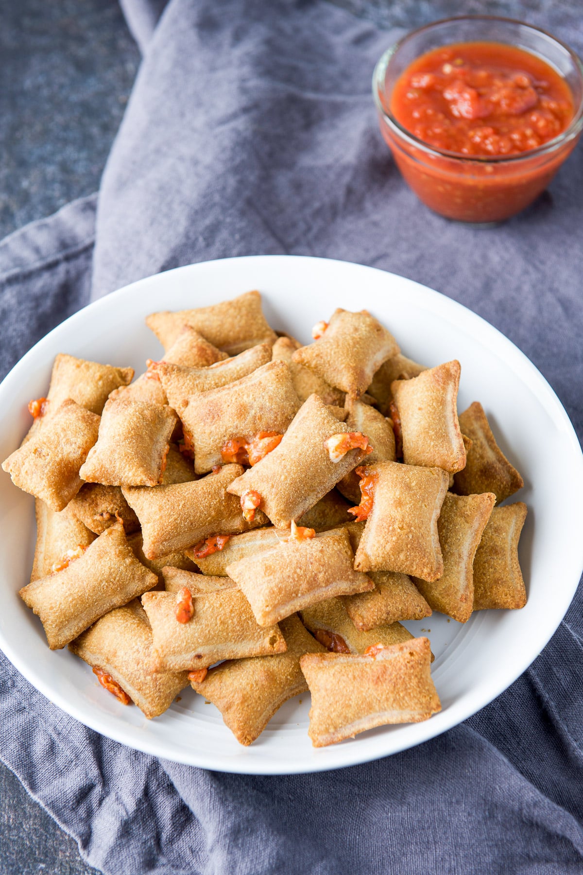 Sauce in a glass bowl behind a bowl of cooked pizza rolls