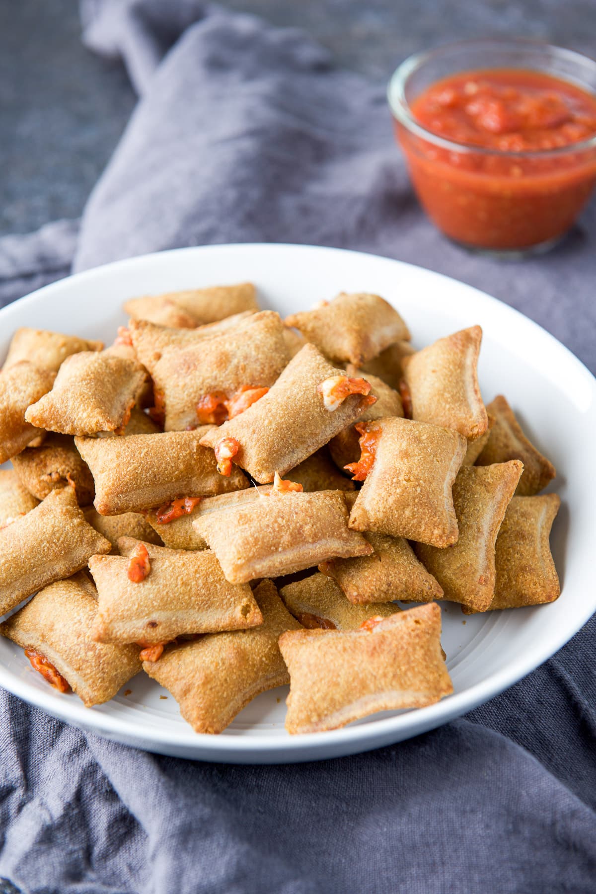a grey napkin with a white bowl on it filled with messy pizza rolls