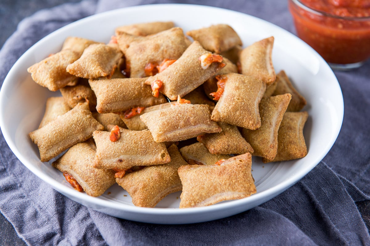 horizontal photo of a white bowl filled with crispy pizza rolls with sauce in the back
