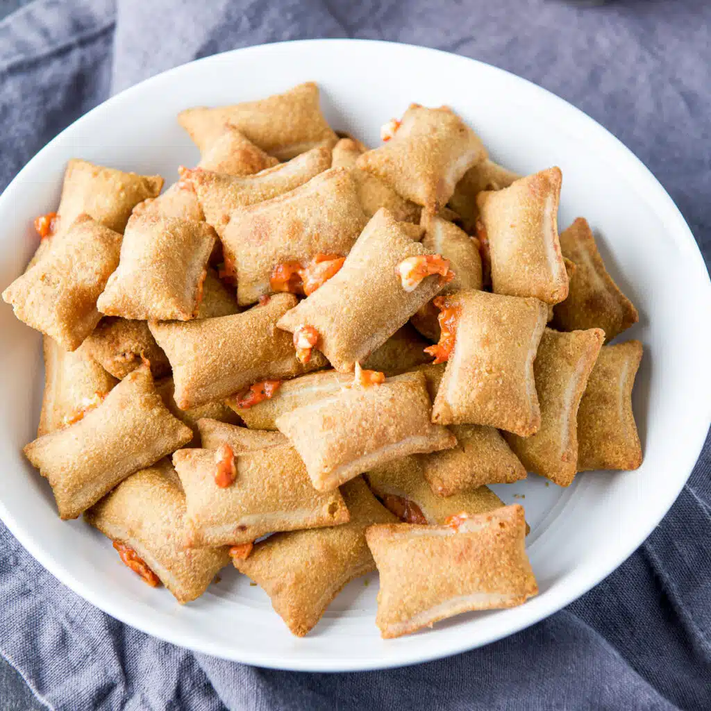 square photo of cooked pizza rolls in a white bowl with cheese and sauce peeking out