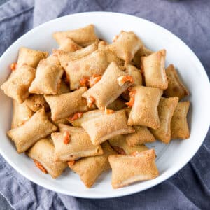 square photo of cooked pizza rolls in a white bowl with cheese and sauce peeking out