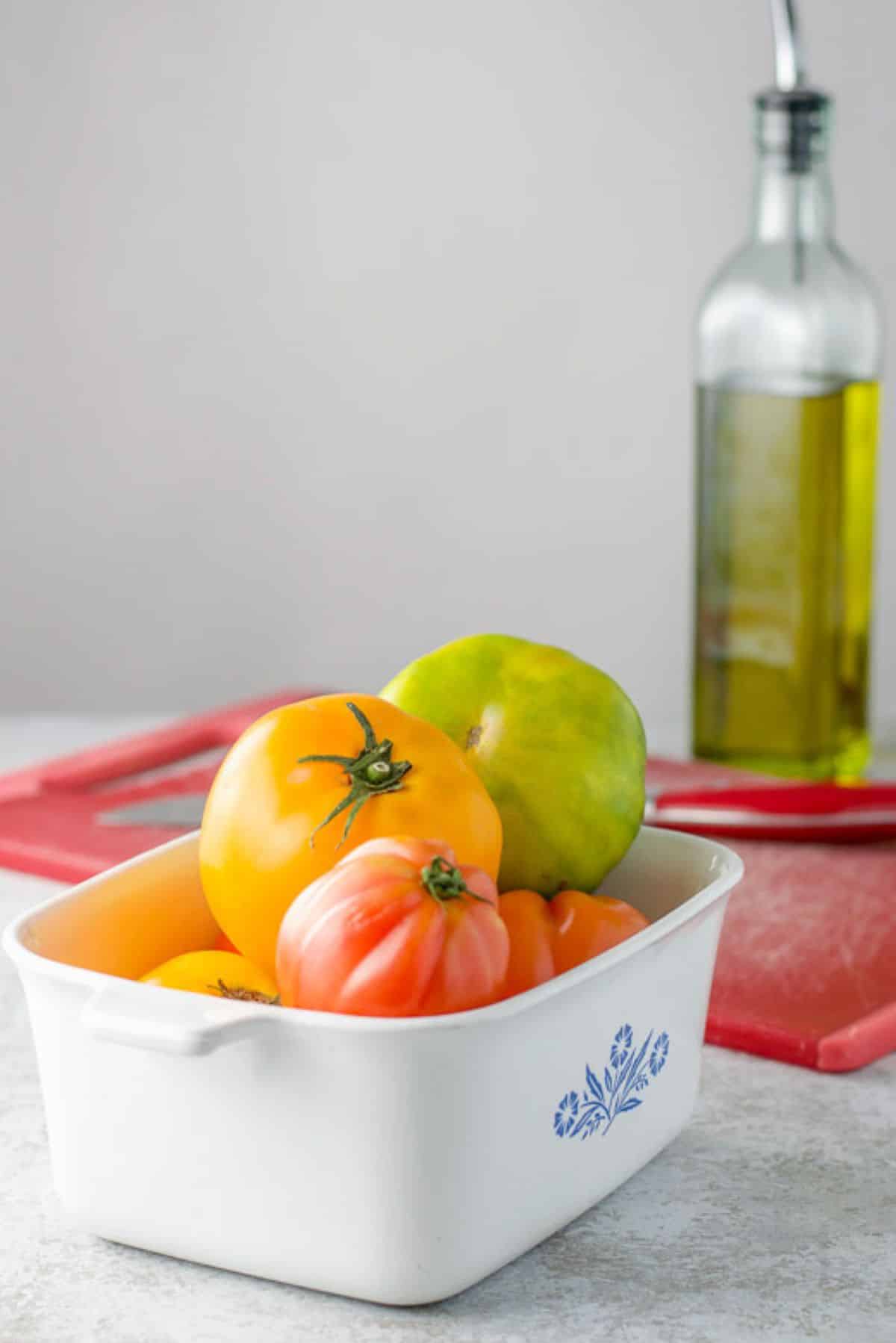 Tomatoes in a bowl with a red board, knife and oil in the background