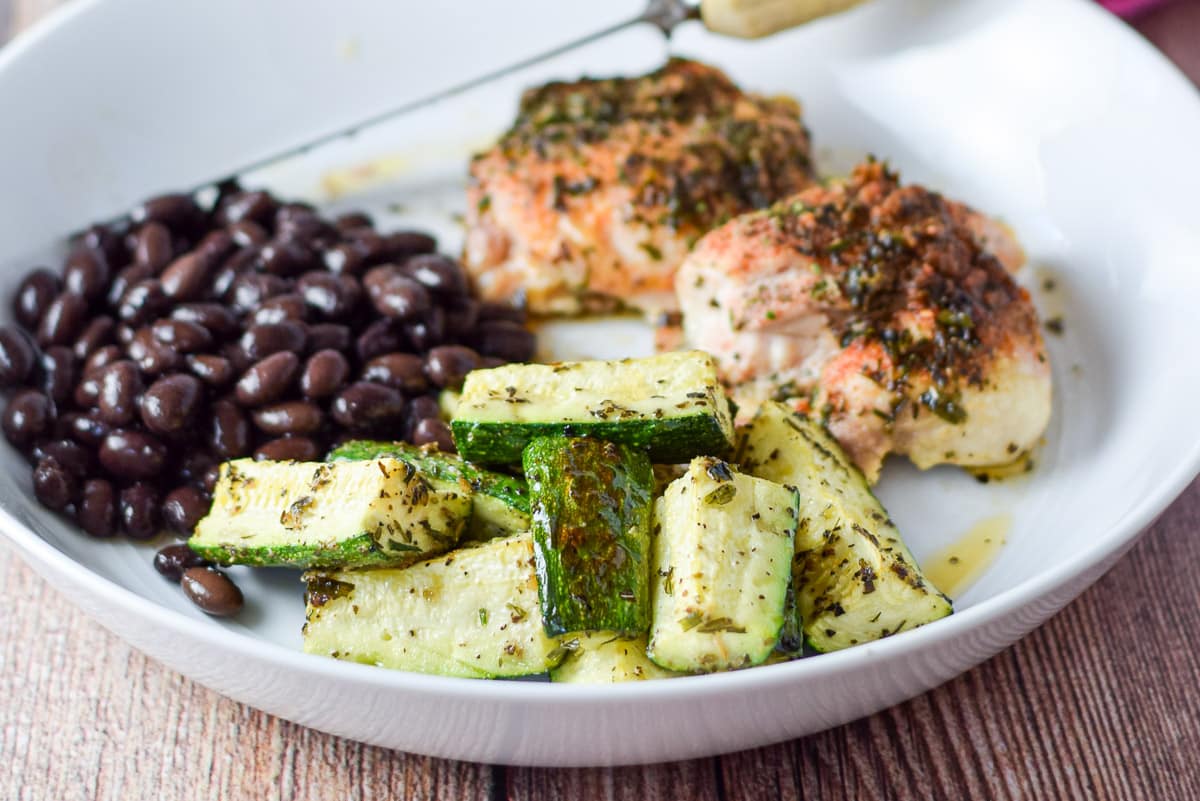 Zucchini, beans and chicken thighs on a deep dish with more zucchini in a bowl in the background