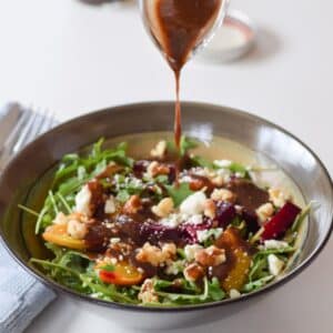 A hand holding a small glass gravy boat pouring the dressing on the salad