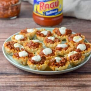 A green plate of the beef and cheese appetizer in front of the jar of sauce - square