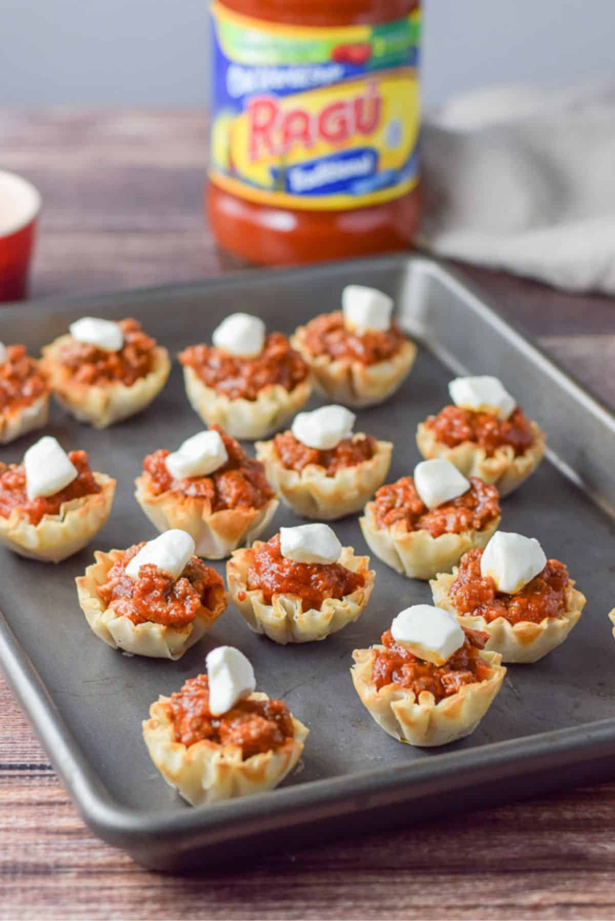 Pearl mozzarella placed on the beef appetizer with the jar of sauce in the background