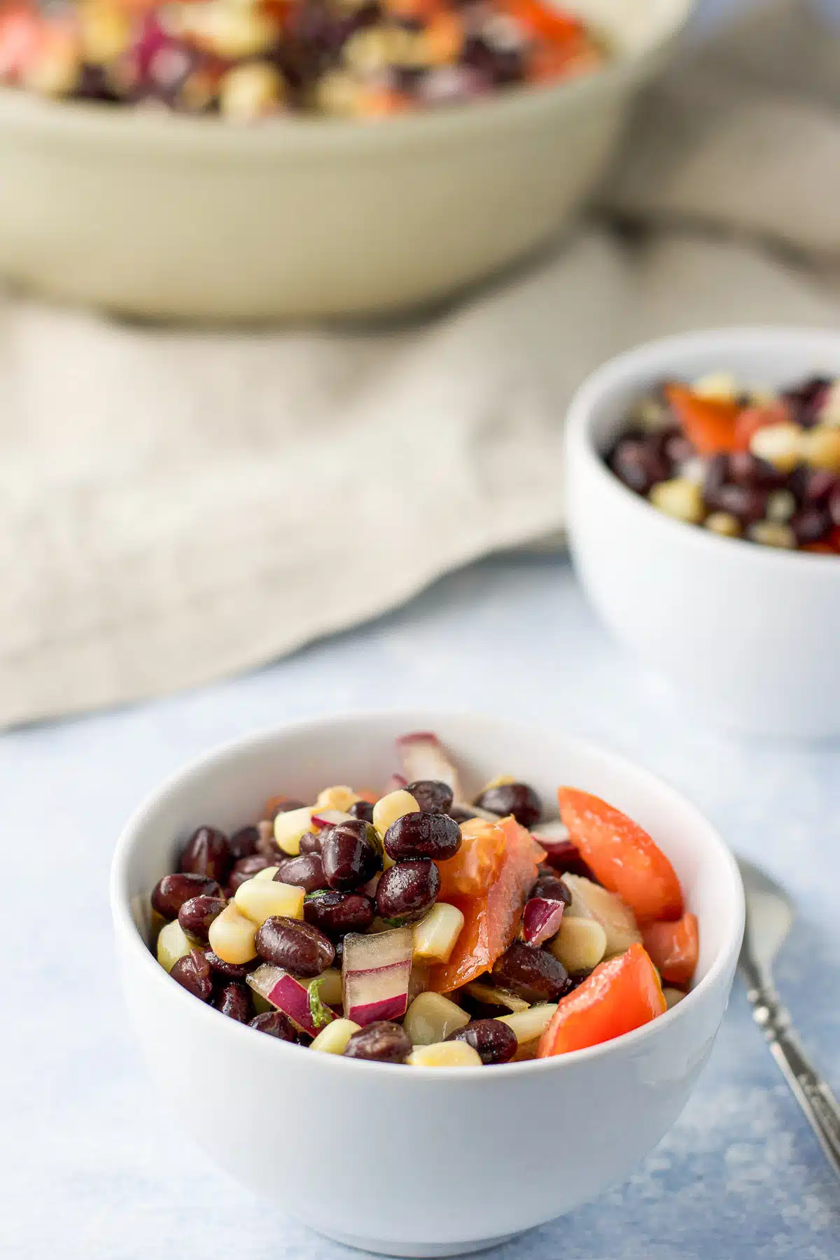 Close up of the two white bowls of bean salad and the big bowl behind them