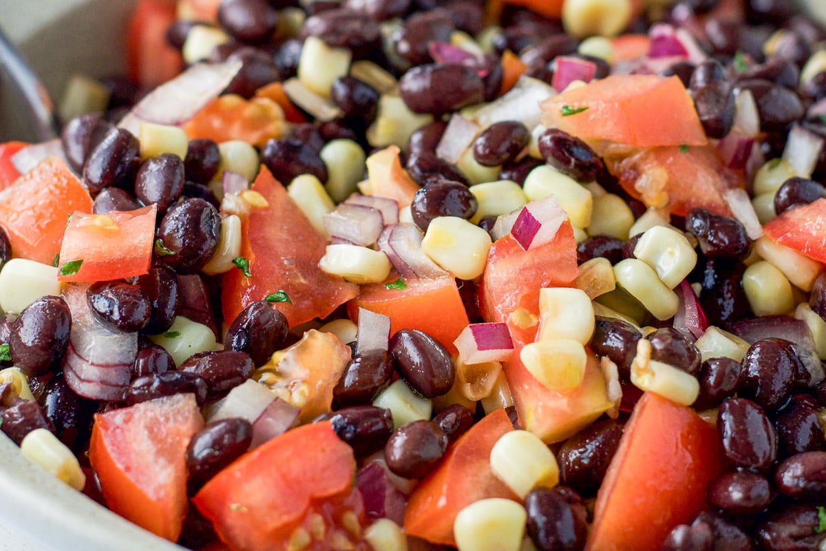 Close up of the big beige serving bowl of black beans, corn, tomatoes and onion