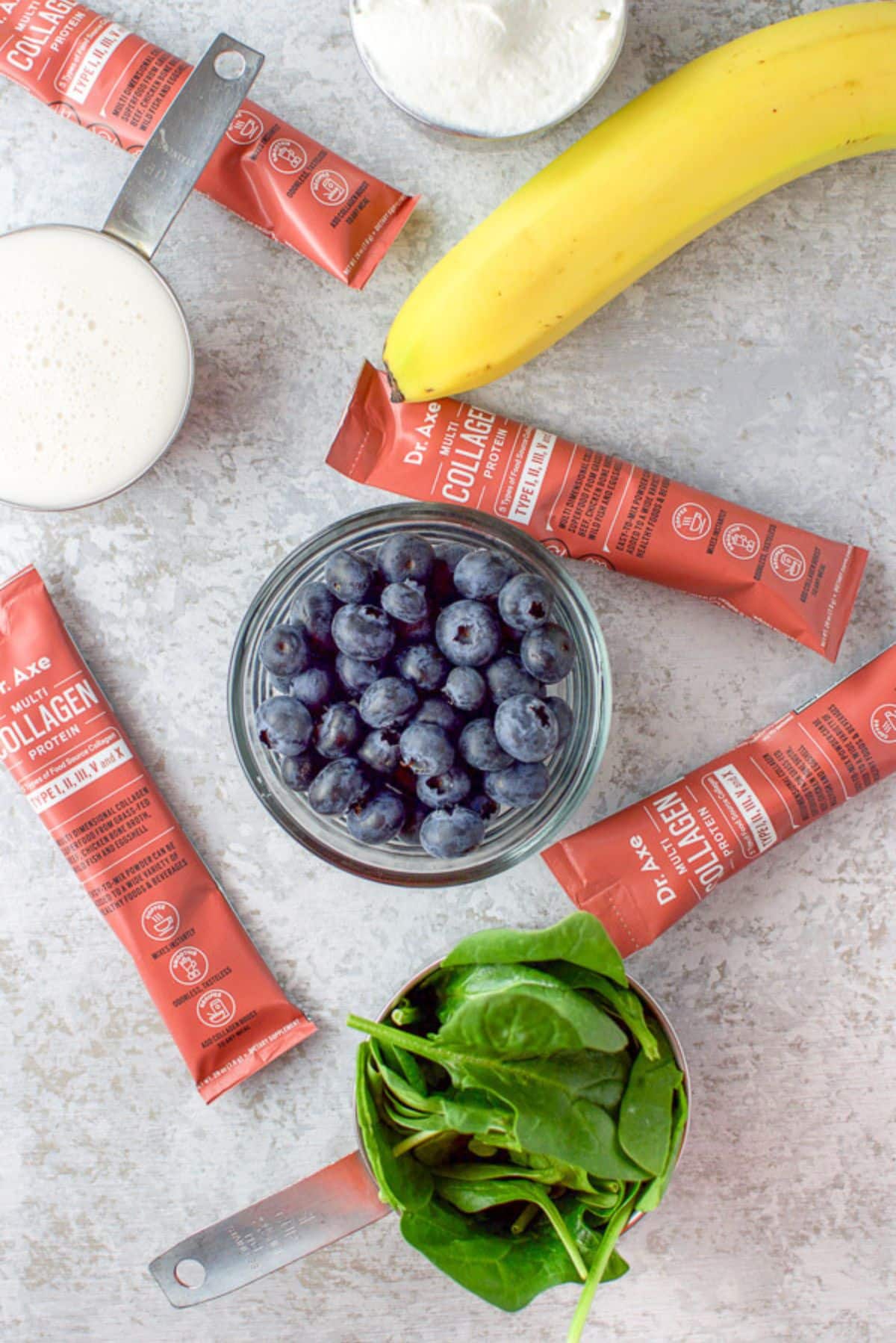 Blueberries, collagen, banana, spinach, milk, and yogurt on a table