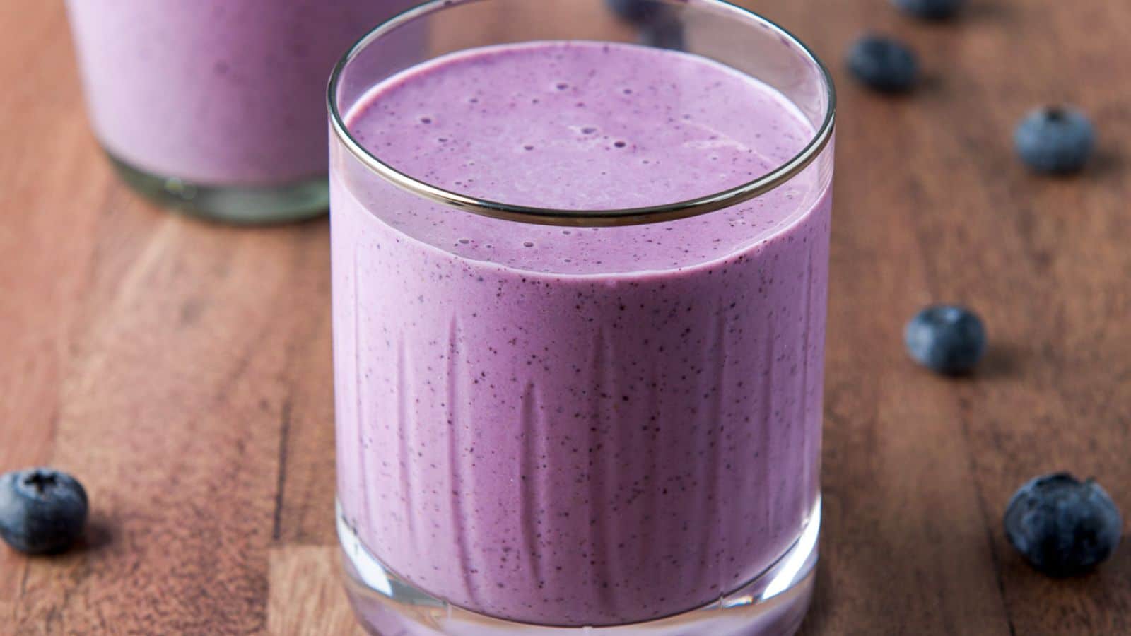 two glasses filled with the blueberry smoothie with blueberries on the wood table