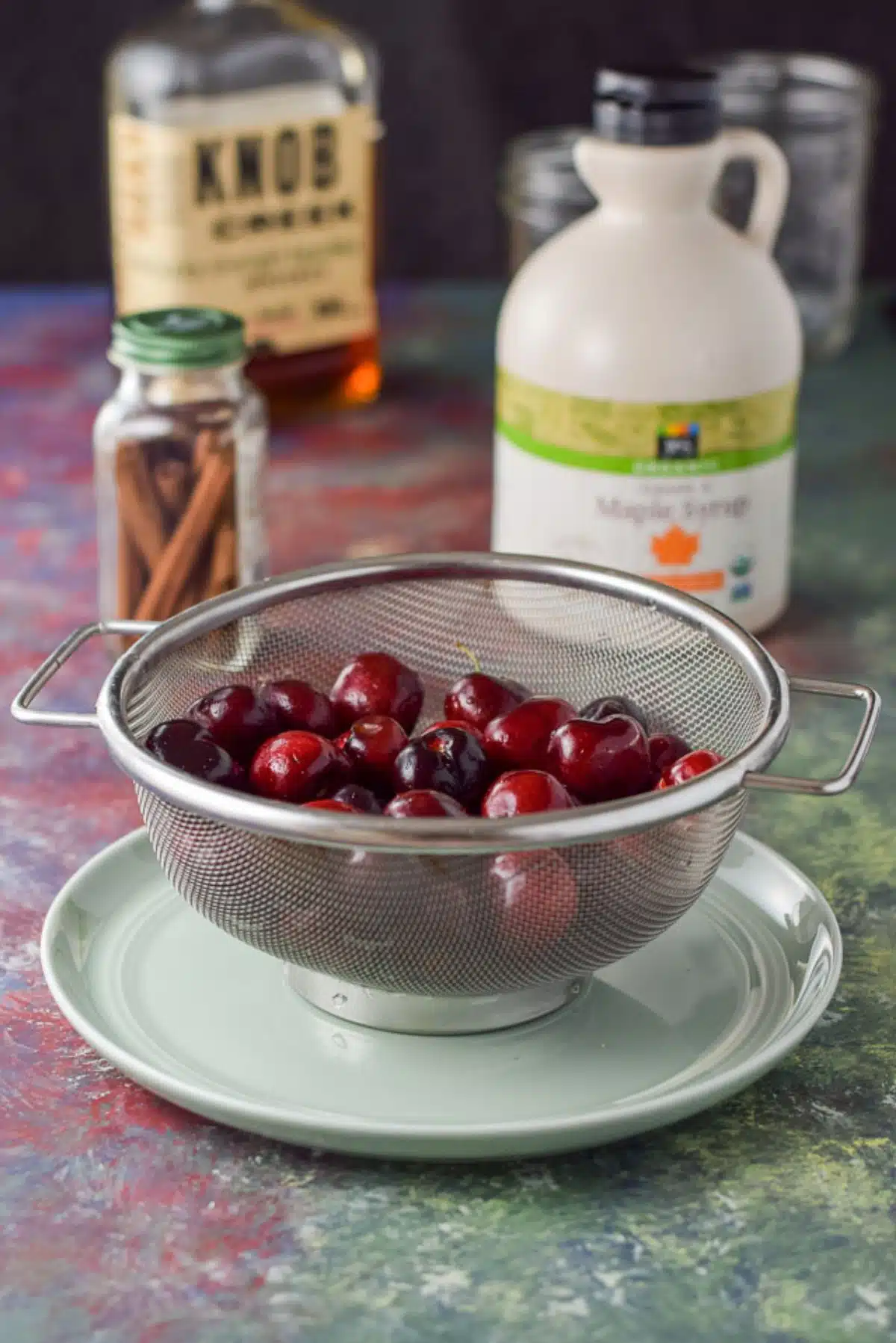 Cherries, cinnamon sticks, bourbon and maple syrup on a colorful table