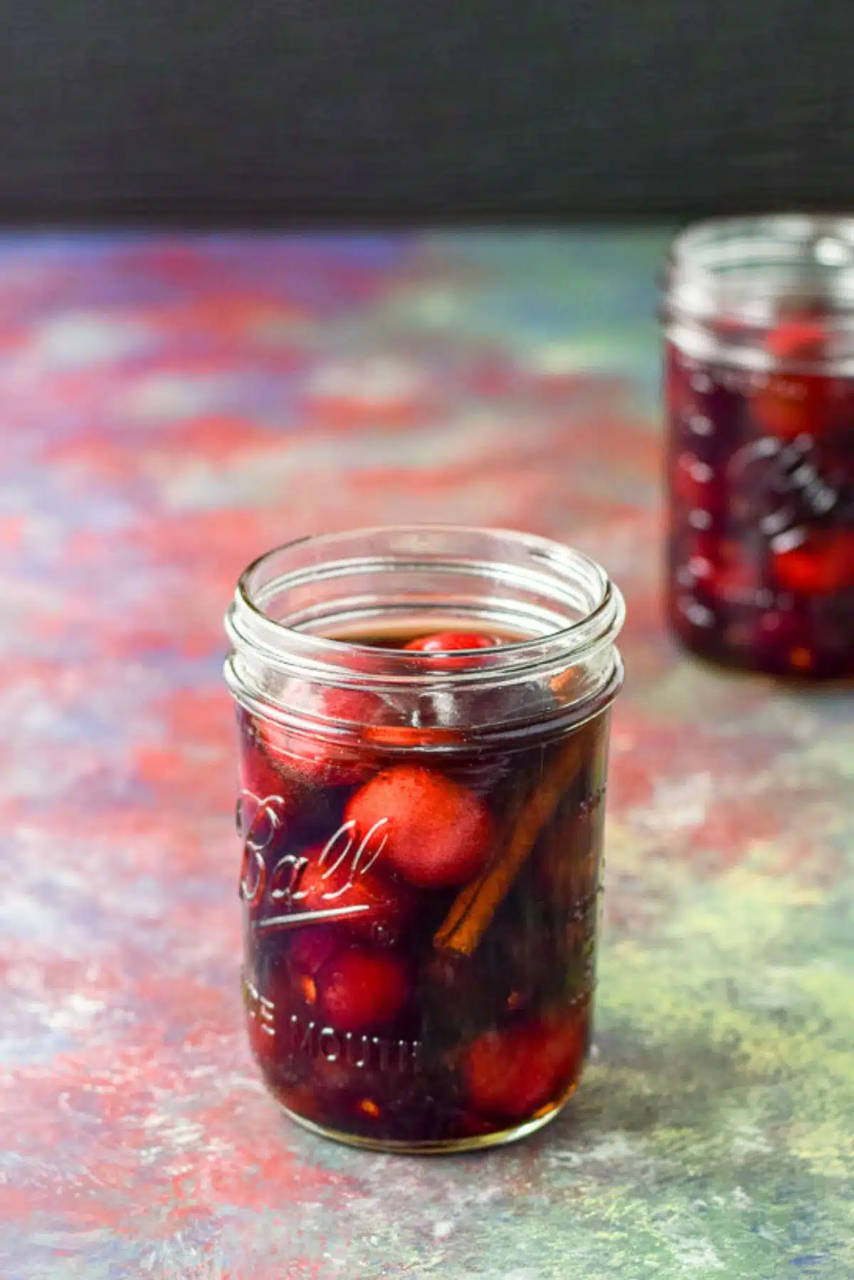 Cherries and cinnamon in bourbon in two jars on a table