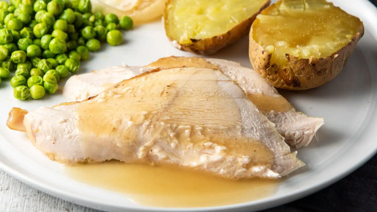 Close view of two slices of turkey with gravy, and potatoes and peas
