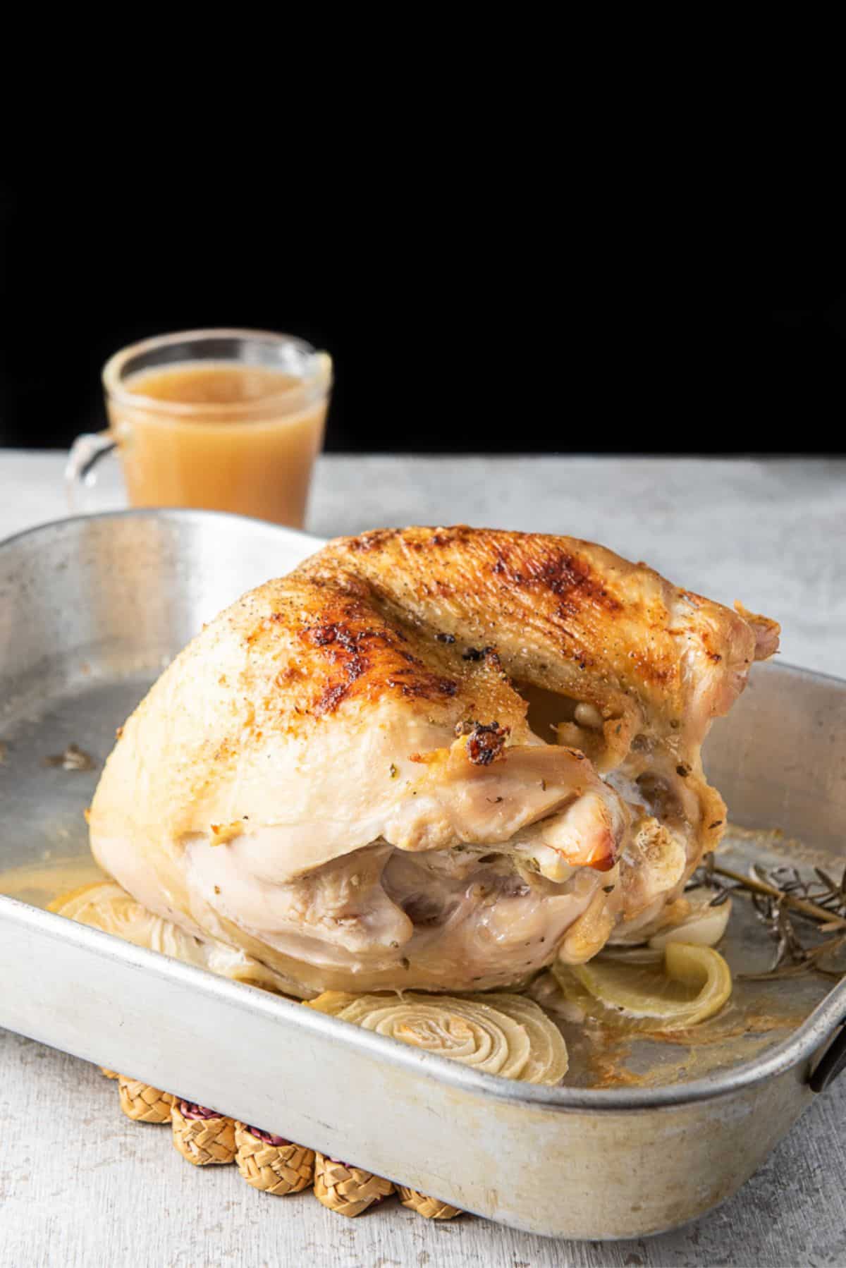 The turkey breast out of the oven with browned skin and gravy in the background