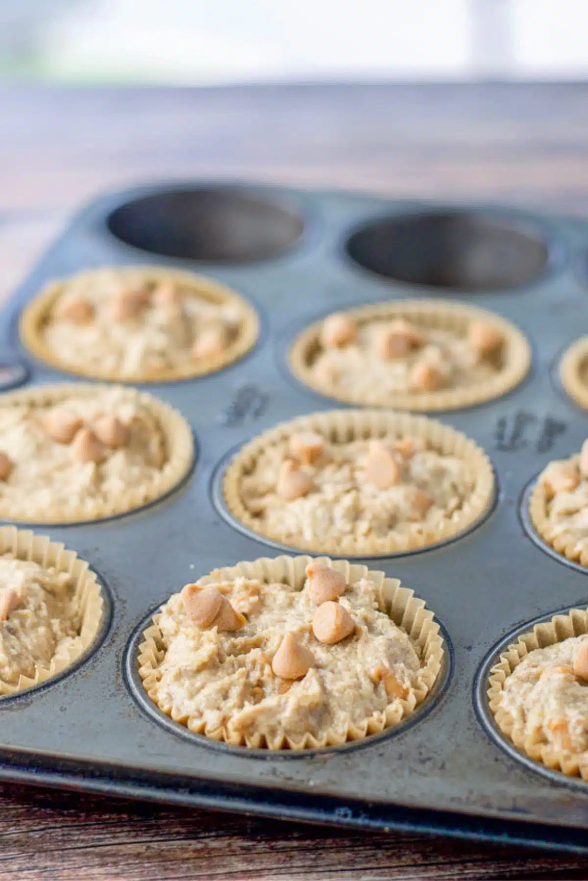 Muffins batter spooned into the muffin tin with butterscotch chips sprinkled on top