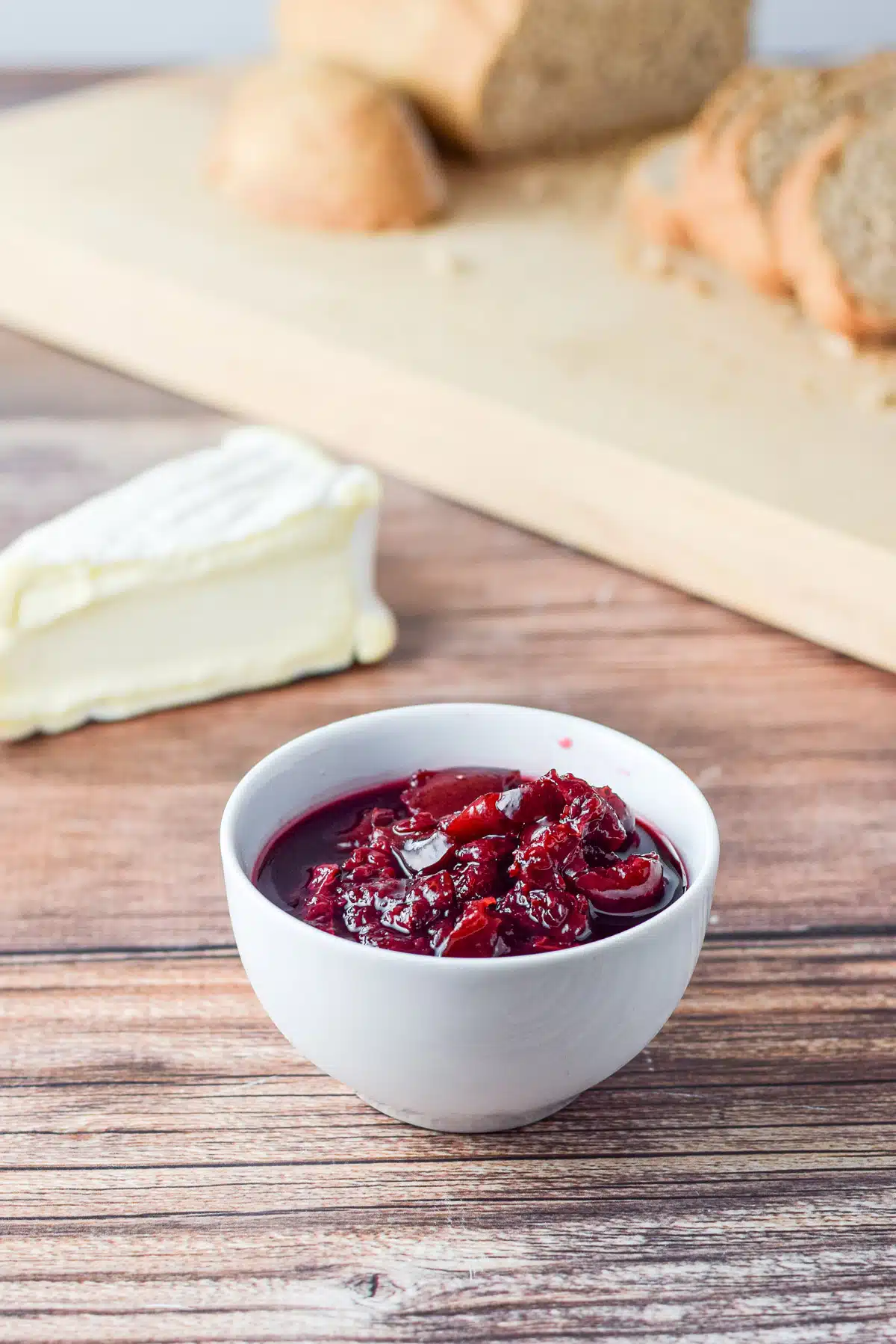 Cherry sauce in a bowl, camembert and bread on a wooden board