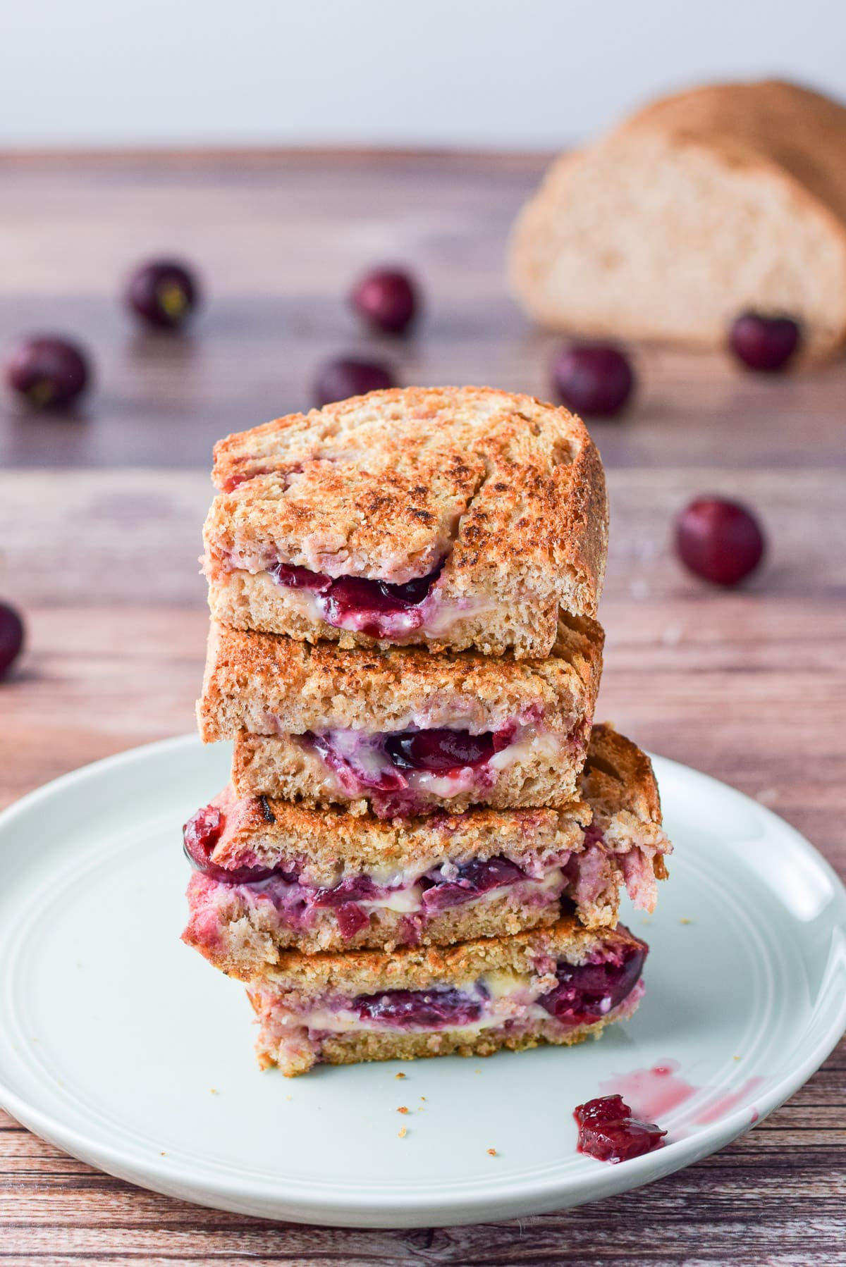 A green plate with a pile of' toasted bread with cheese and cherries peeking out