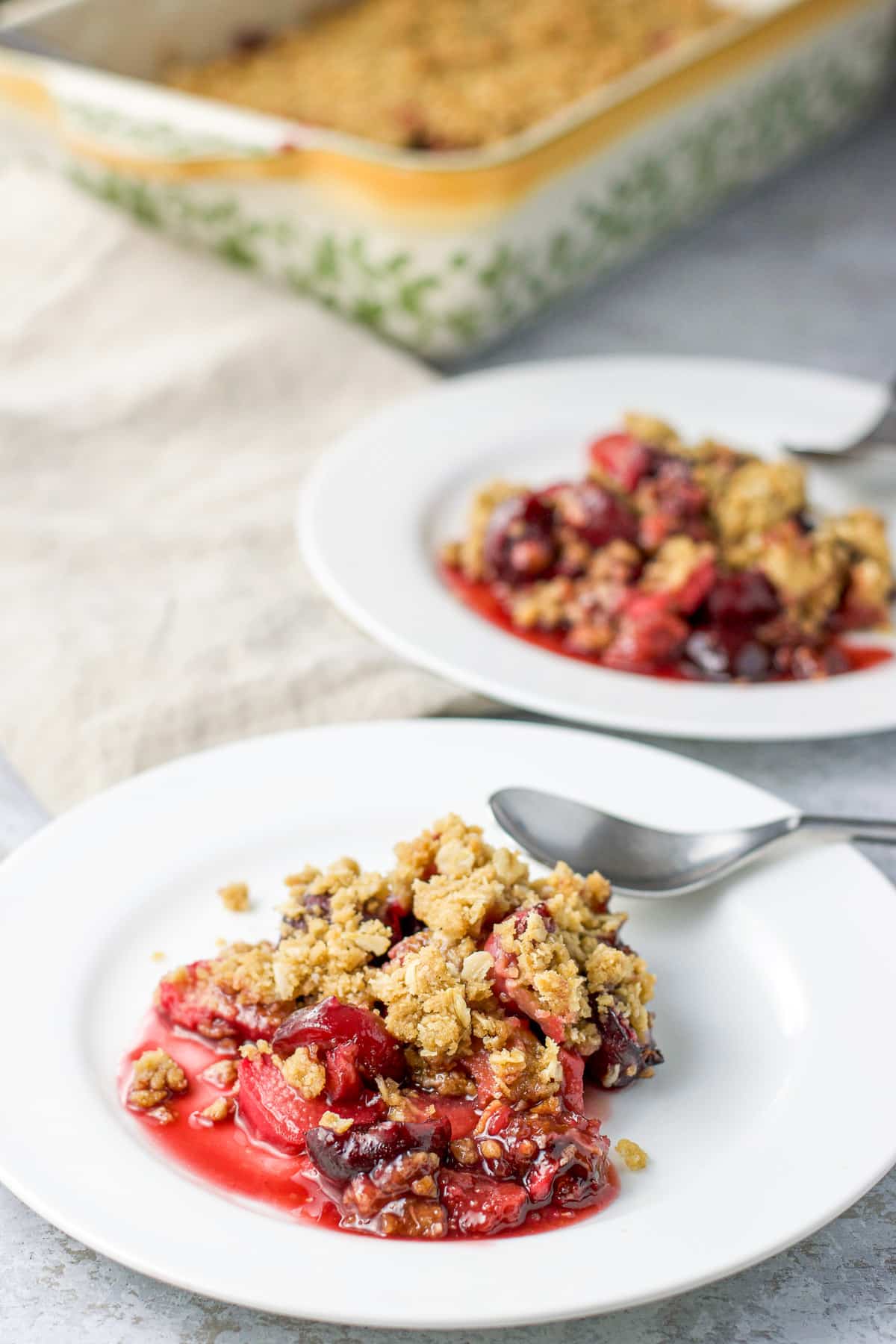 A pan of the dessert behind the two plates with the crisp on it along with spoons