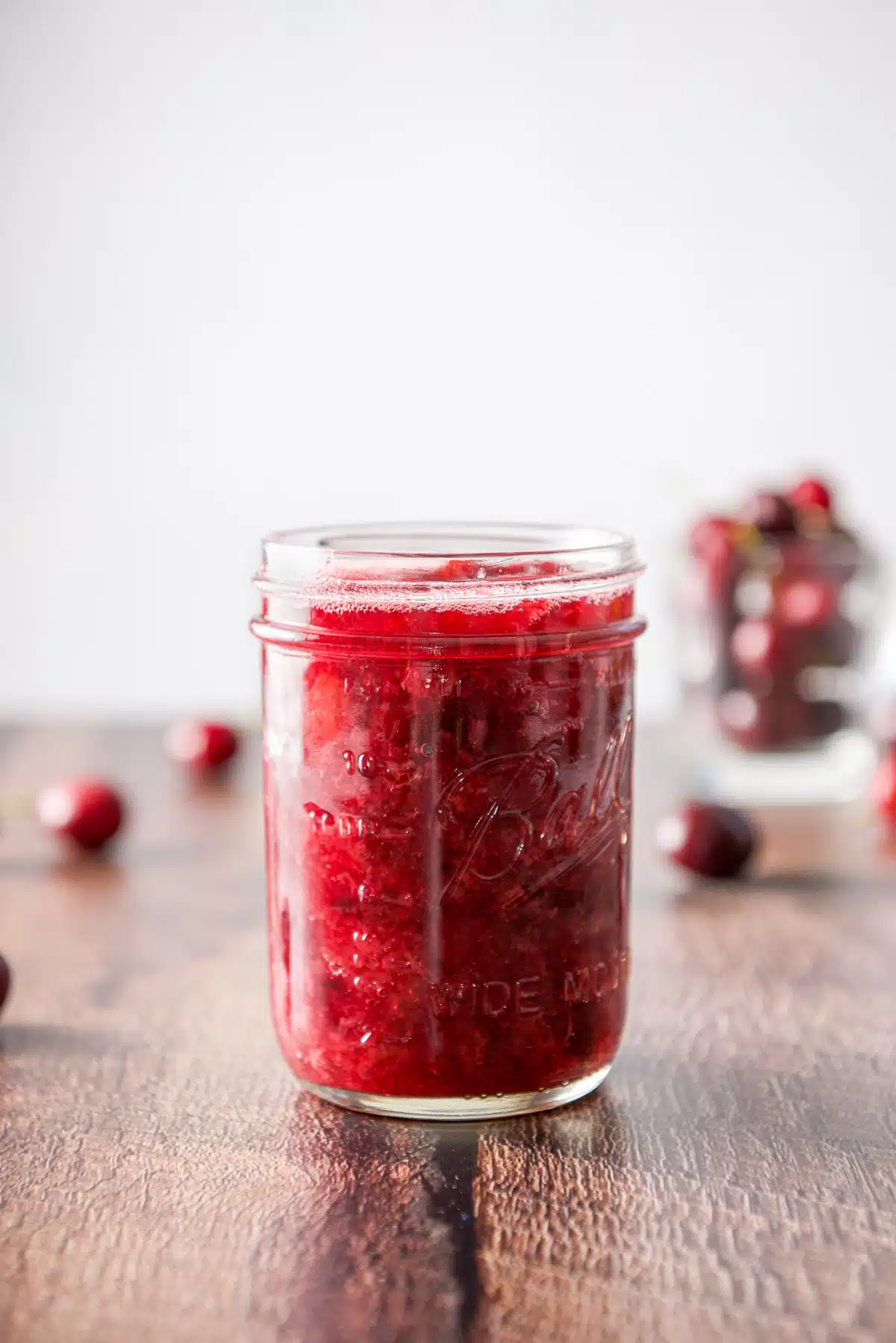 Vertical view of the sauce in a jar with cherries in the background