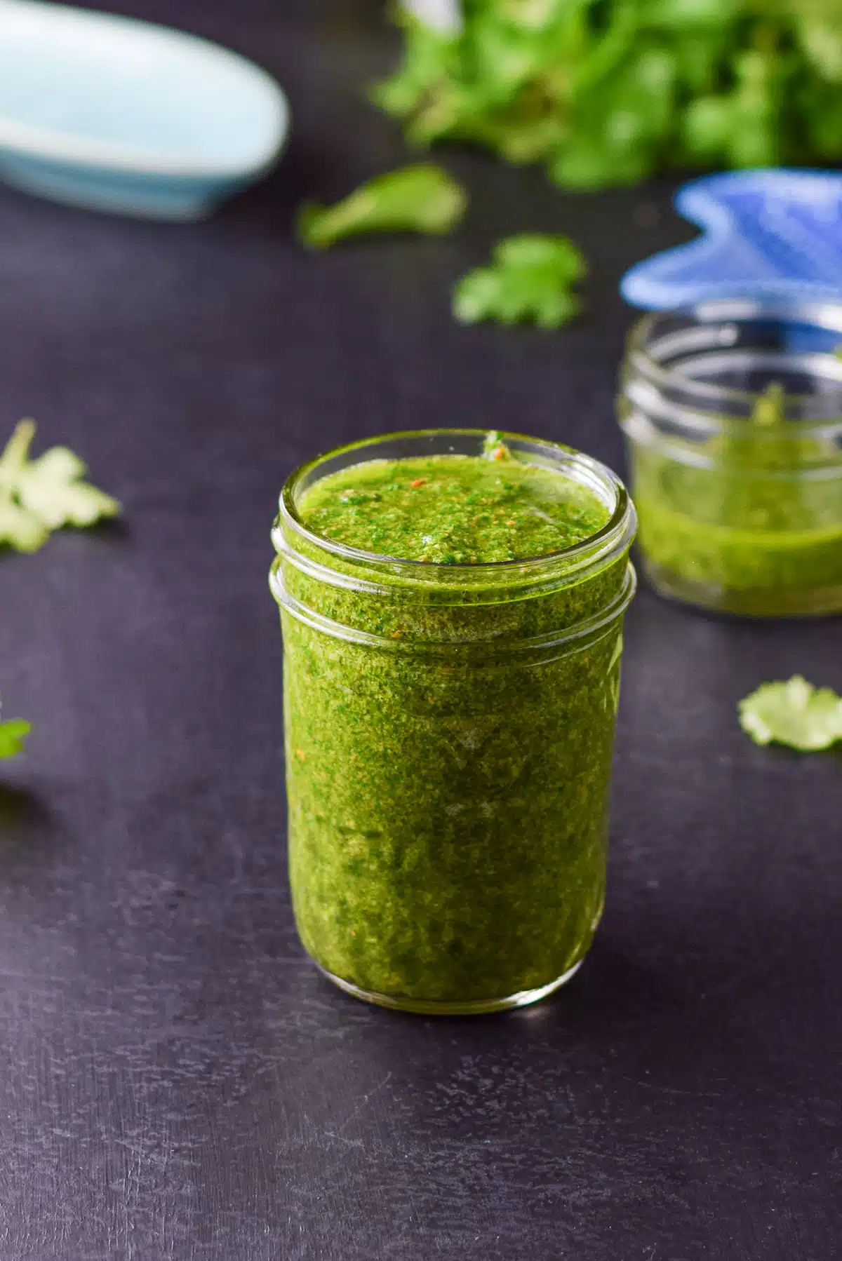 A ball jar full of chimichurri with parsley leaves in the background
