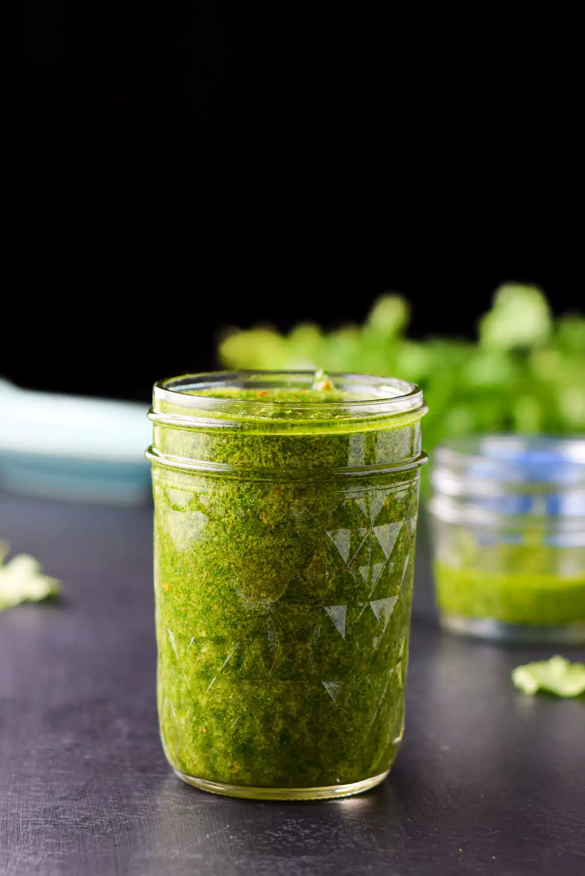 Vertical view of a all jar full of a green sauce with parsley leaves in the background