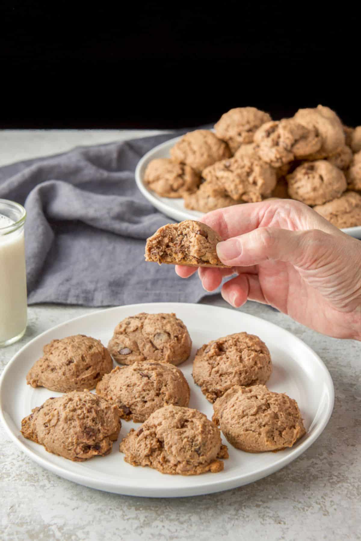 A bite taken out of one of the cookies. It is being held over a plate of cookies