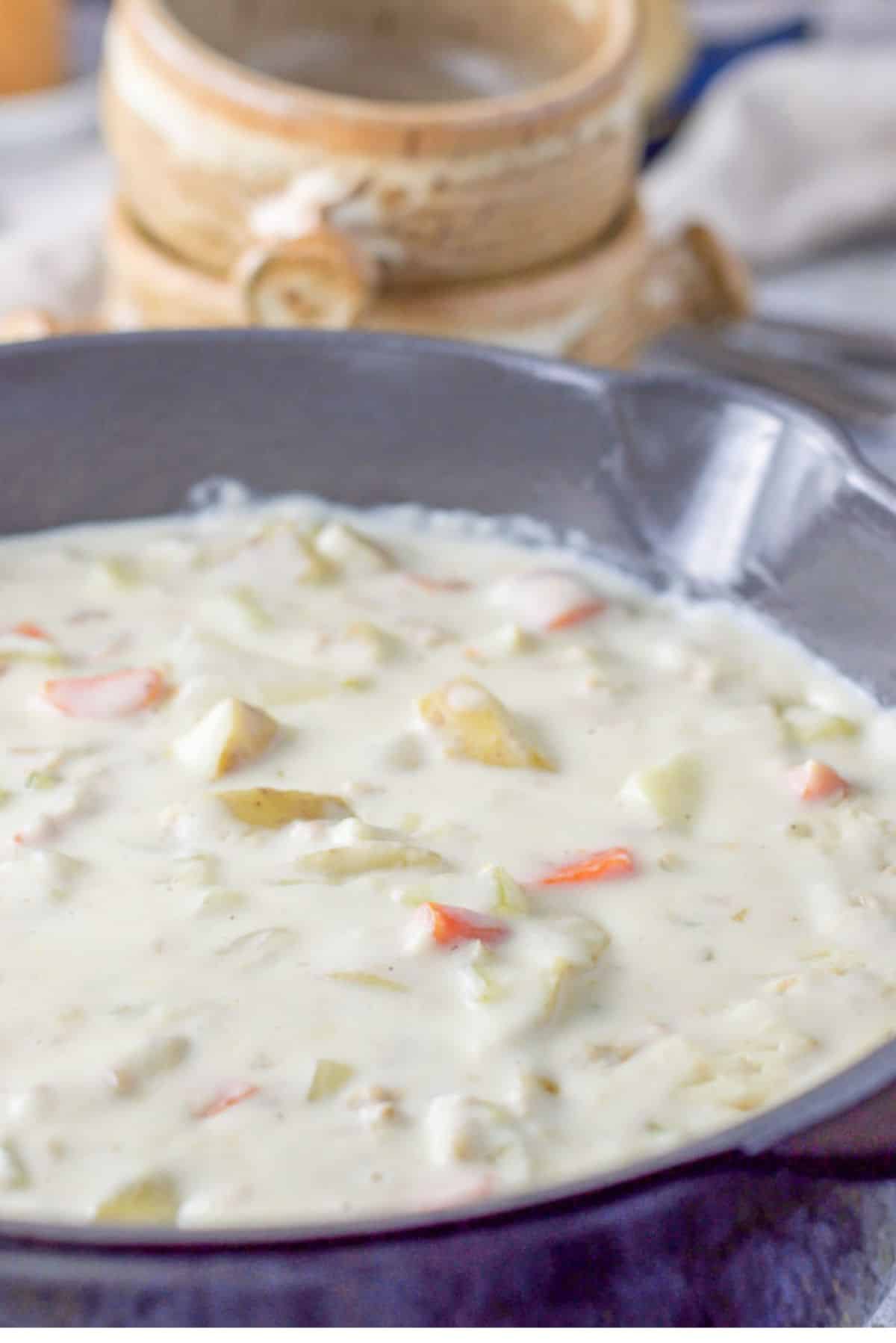 Close up shot of a pan full of the chowder with some bowls in the background