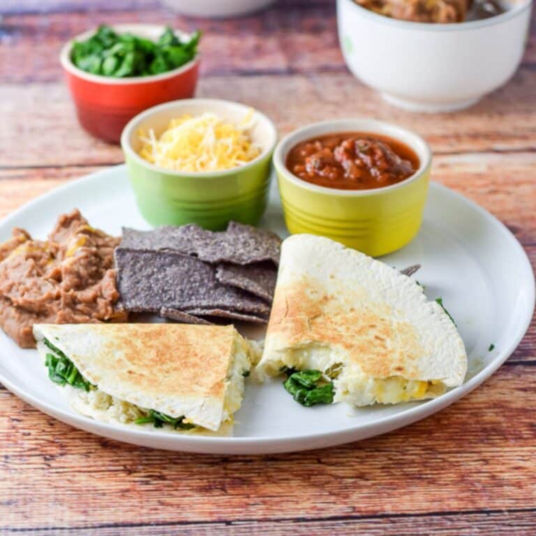 A white plate with a bite taken out of a quesadillas with chips, beans, cheese and salsa - square