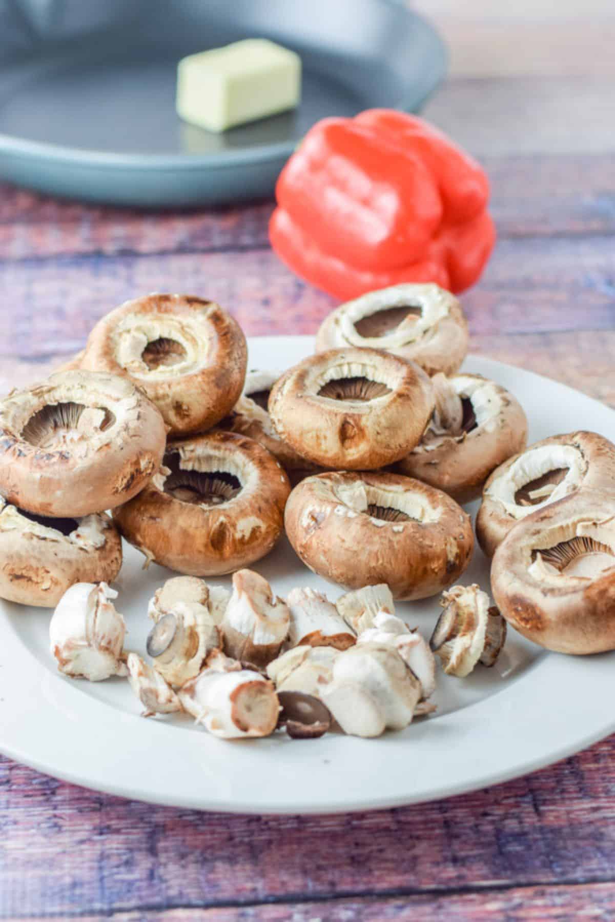 Mushrooms with the stems taken out on a white dish with a red bell pepper and a cast iron pan