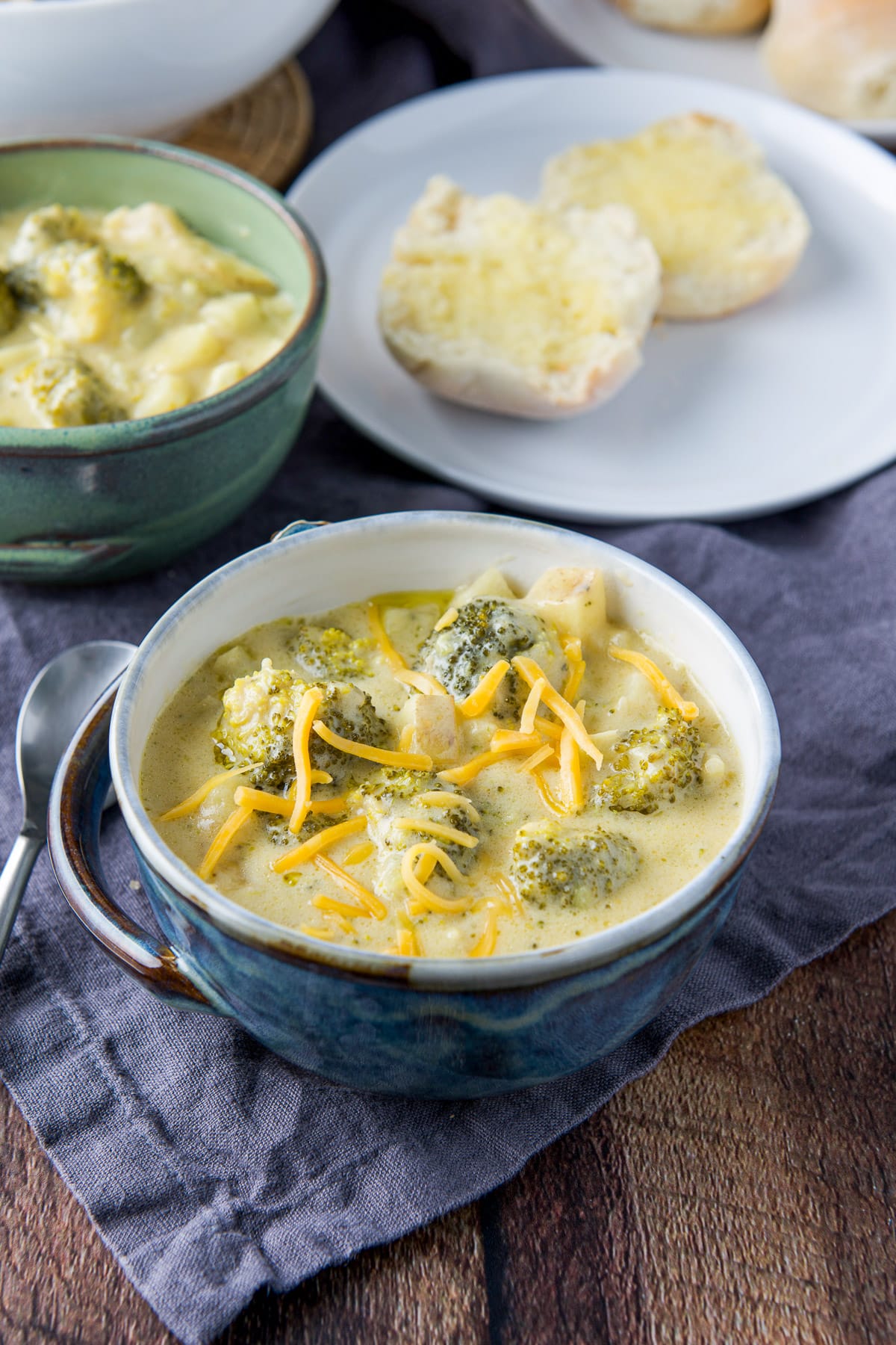 Blue and green bowls filled with the chunky soup with a roll with butter on a plate