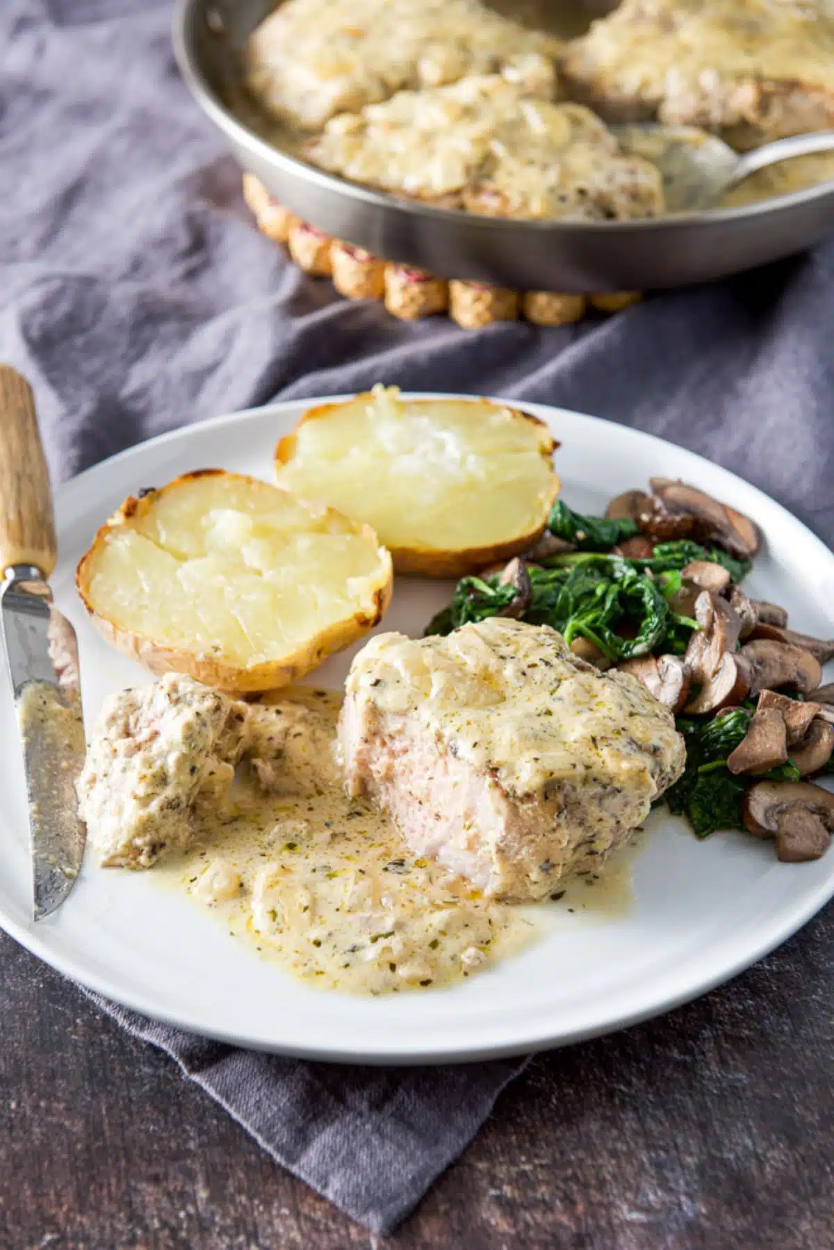 the pork chop cut with the sauce in front of it and mushrooms, spinach and baked potatoes