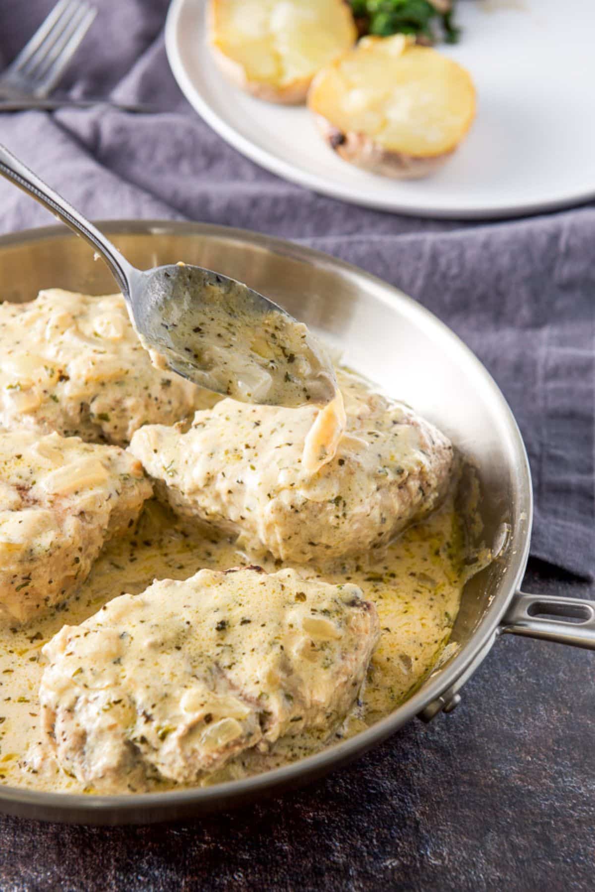 A spoon dribbling some sauce over the pork chops in a stainless steel pan