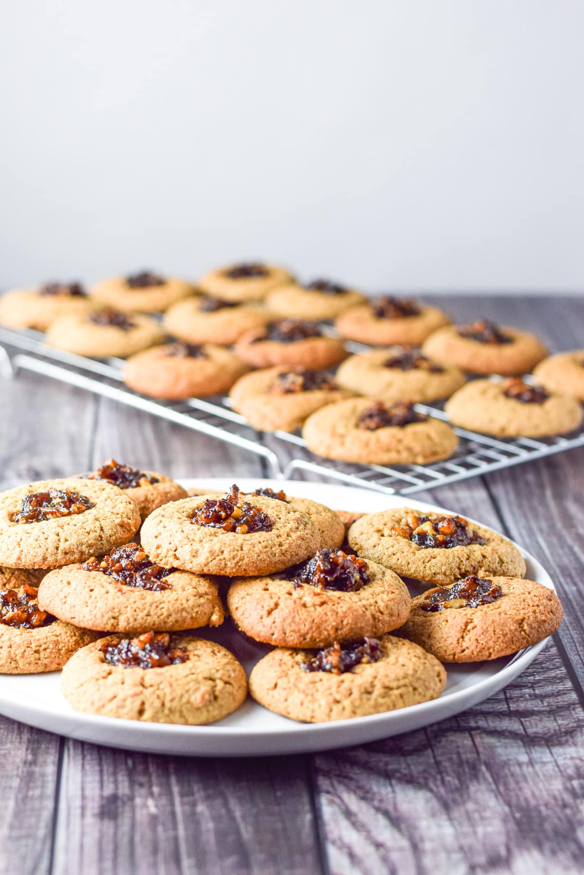 A round plate of the date cookies all stacked up and a wire rack of cookies in the background