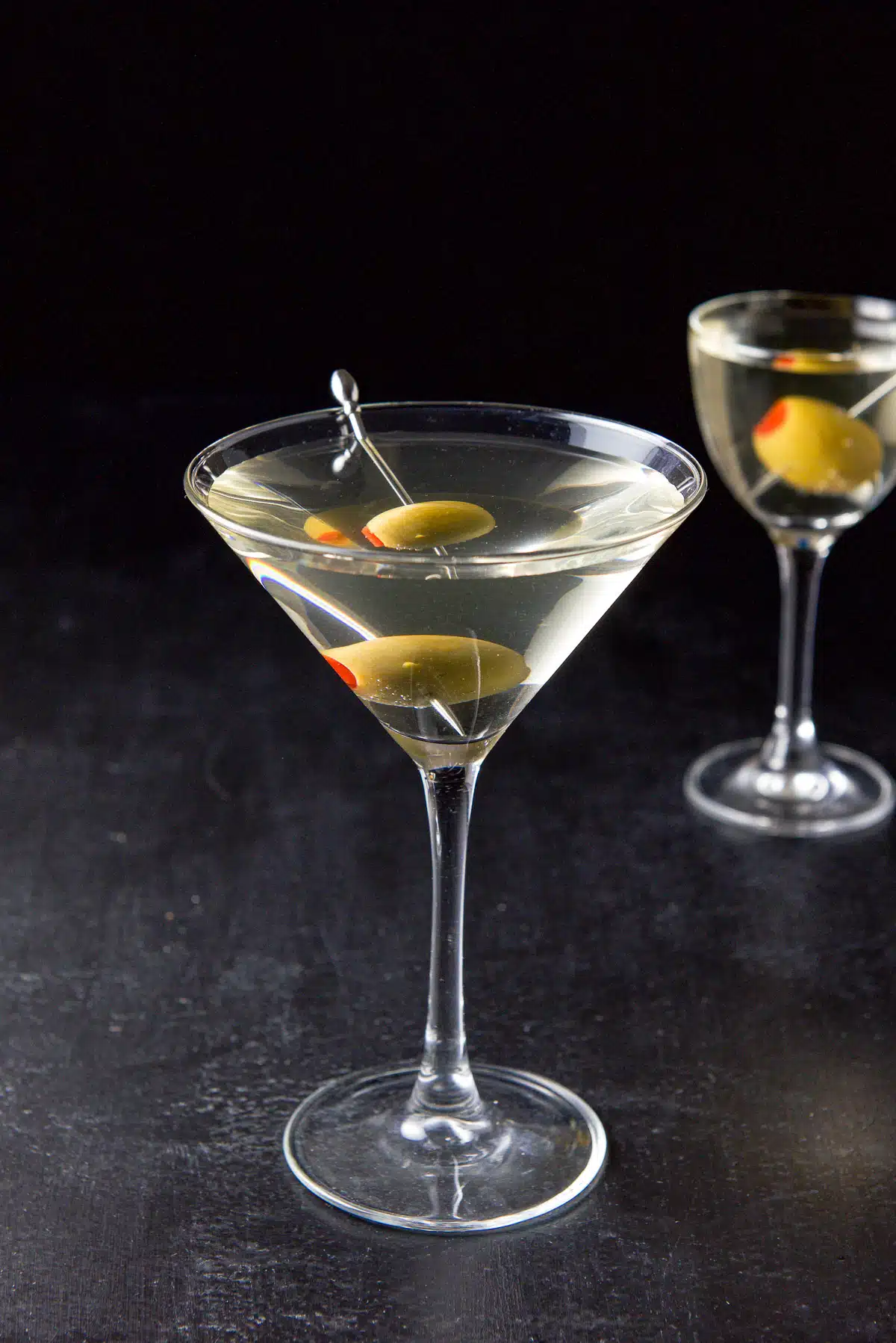 Two martini glasses filled with the martini with olives on picks as garnish