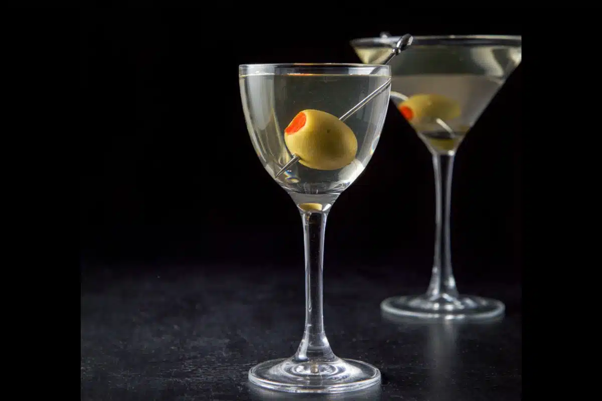 Vertical view of the smaller glass with the martini with a big olive in it. Regular martini glass in the background