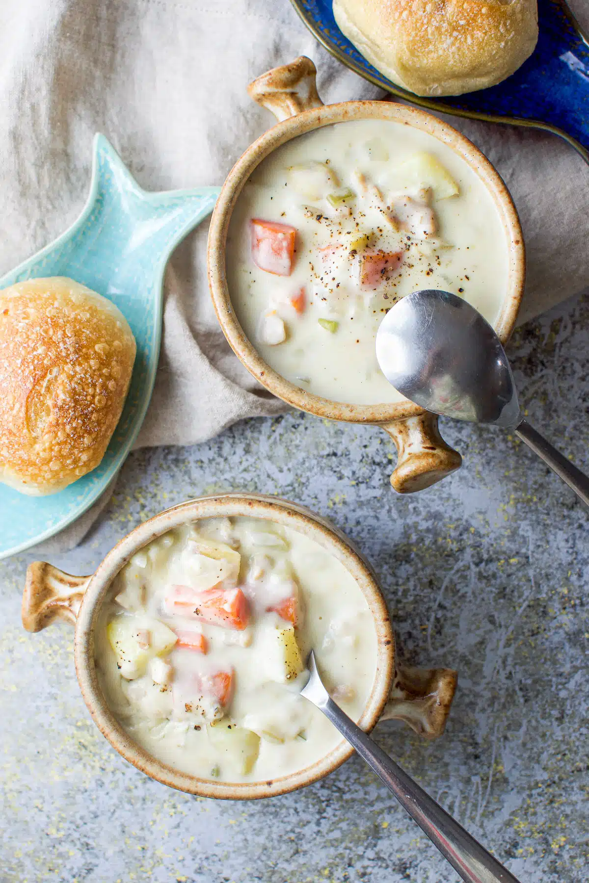 Overhead shot of the clam chowder with the spoons in the crocks and rolls in little fish dishes