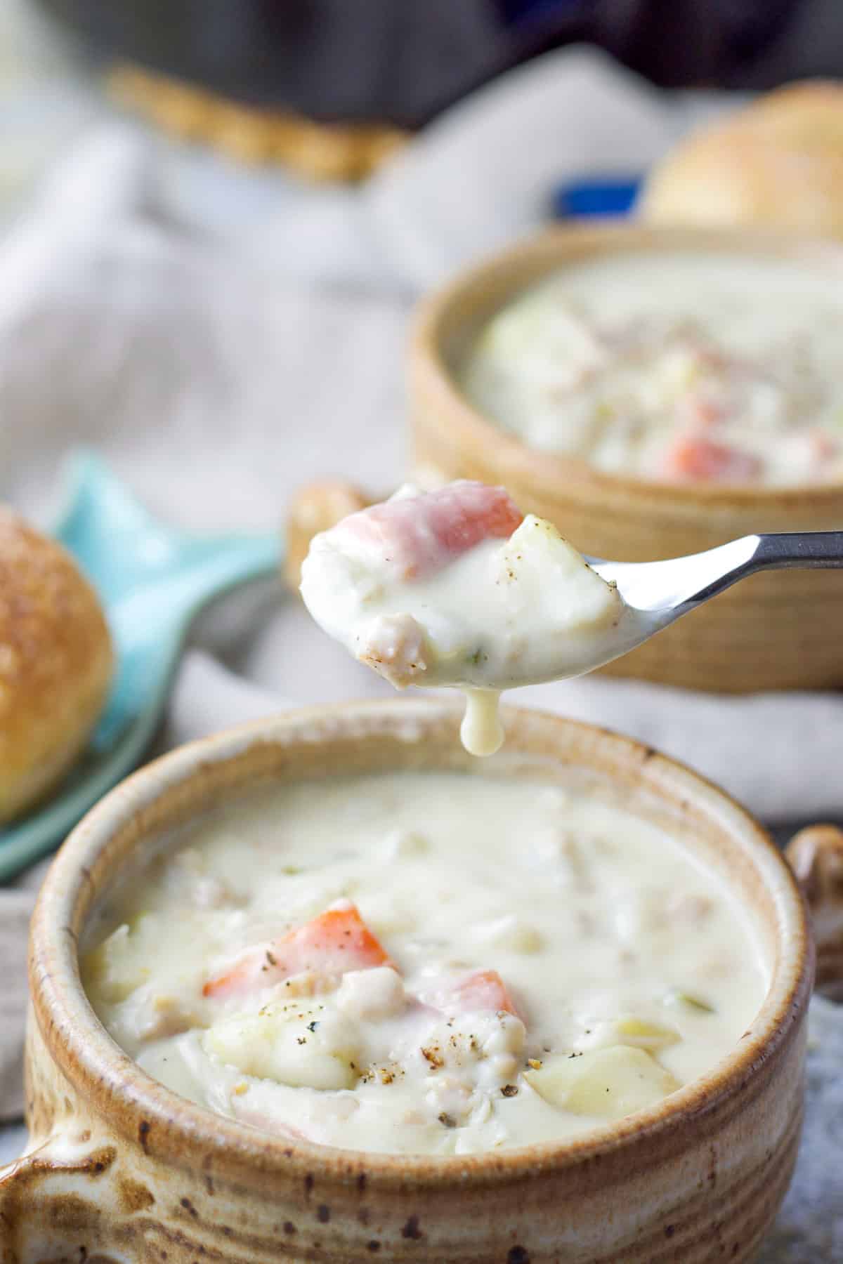 A spoonful of chowder with a drip hanging off the spoon with another crock in the background