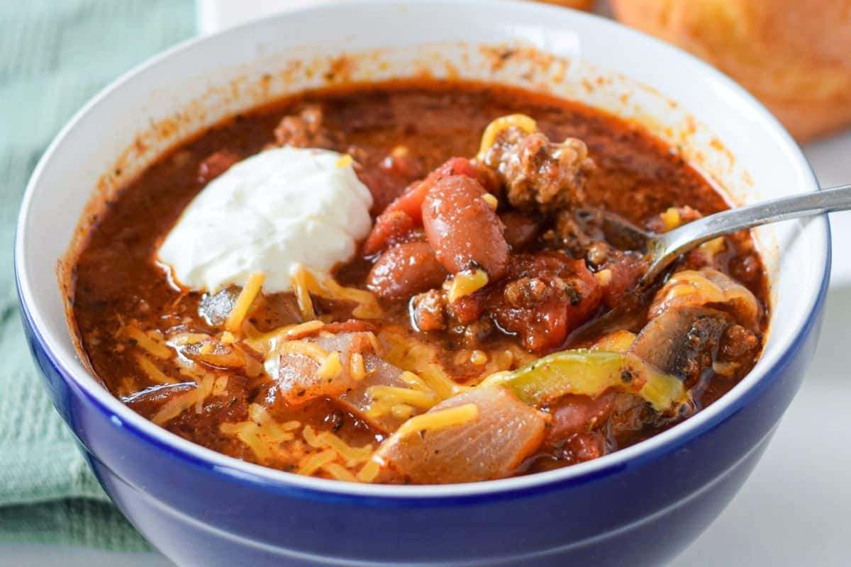 a blue bowl with chili in it, along with cheese and a dollop of sour cream
