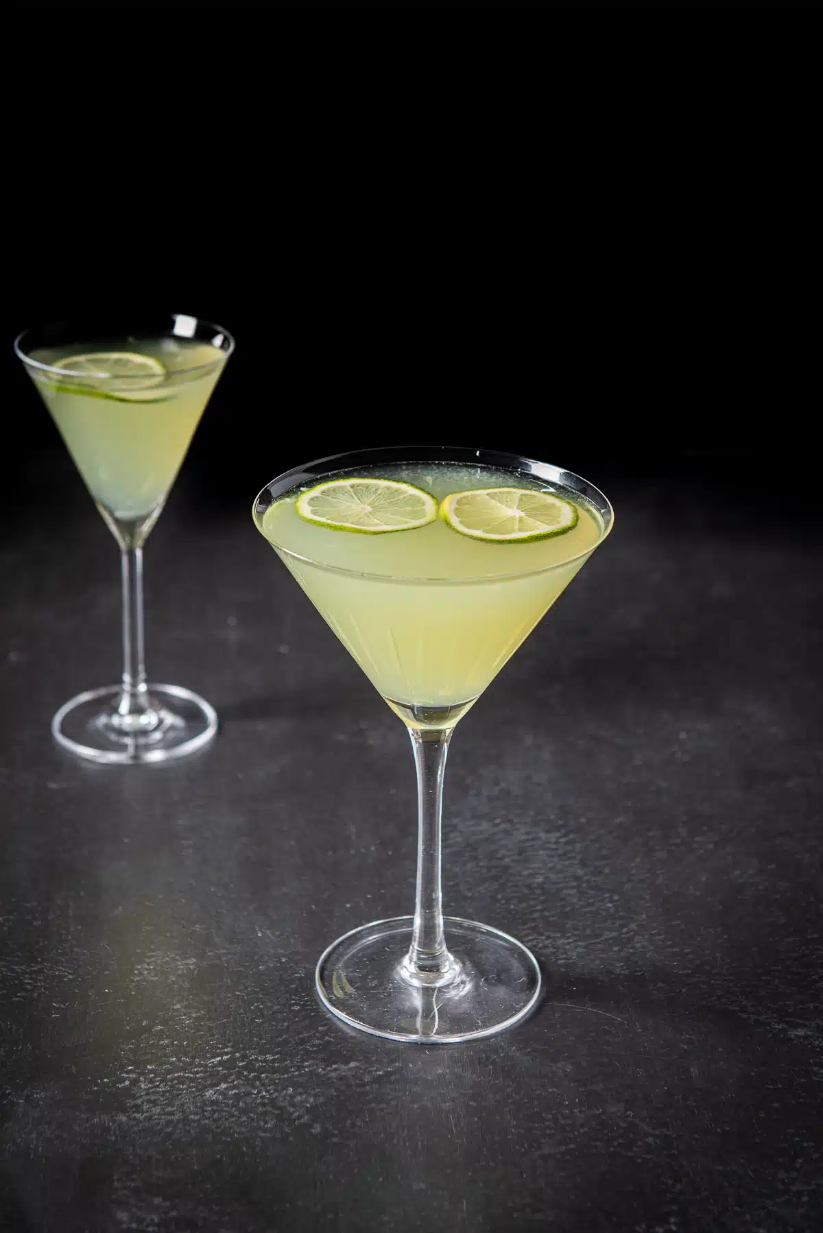 Two glasses filled with a lime cocktail with two thin lime wheels floating