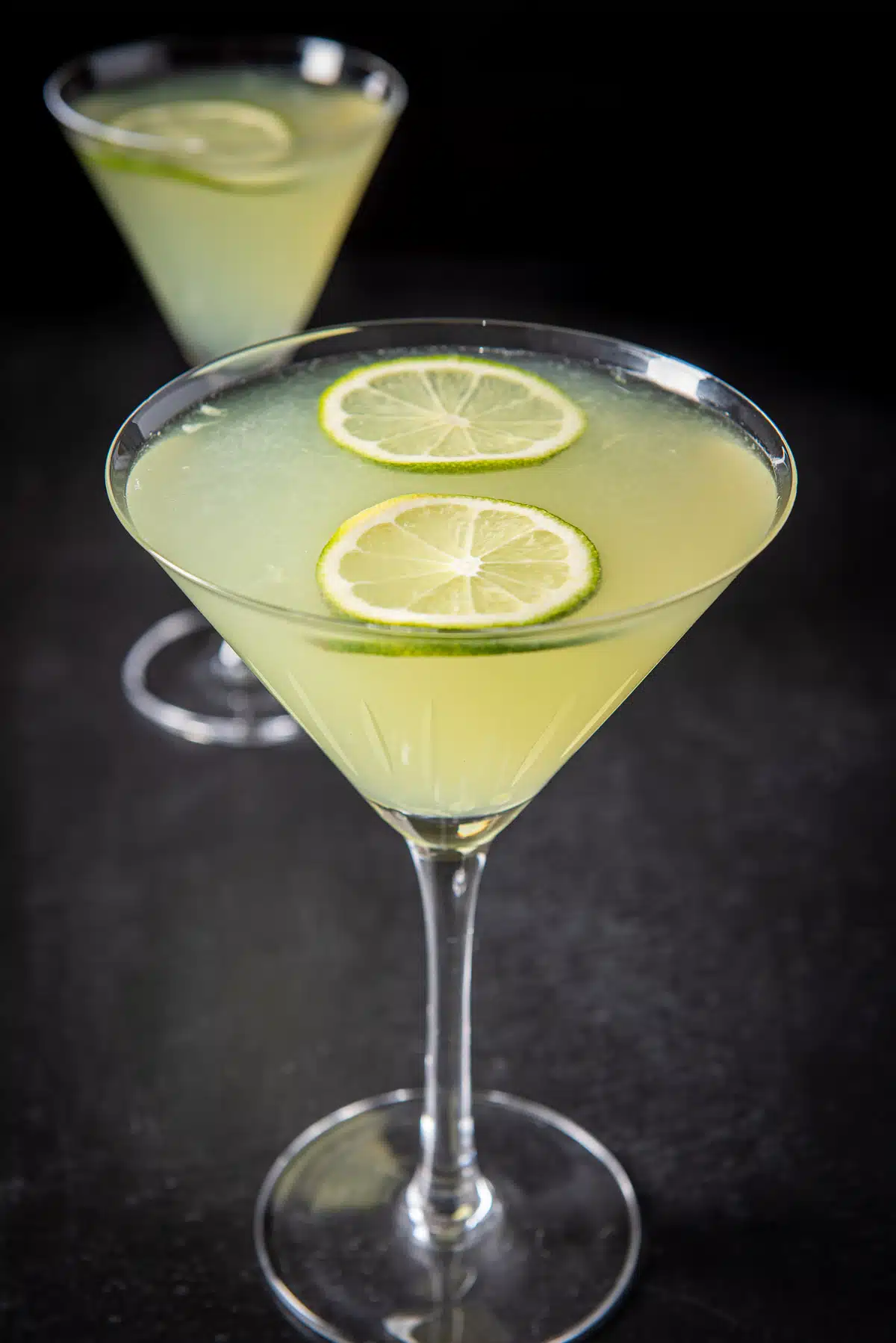 Close up of a lime cocktail in martini glasses with limes floating on the top