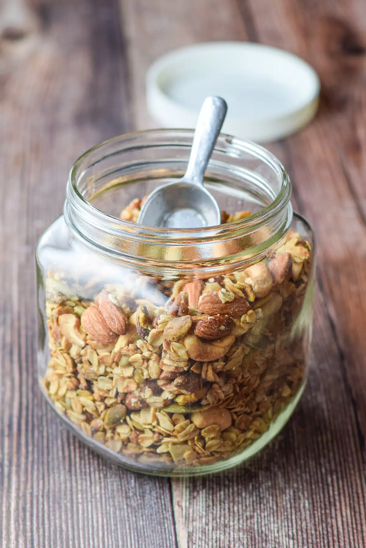 A large glass jar filled with nuts and granola with a small scoop in it