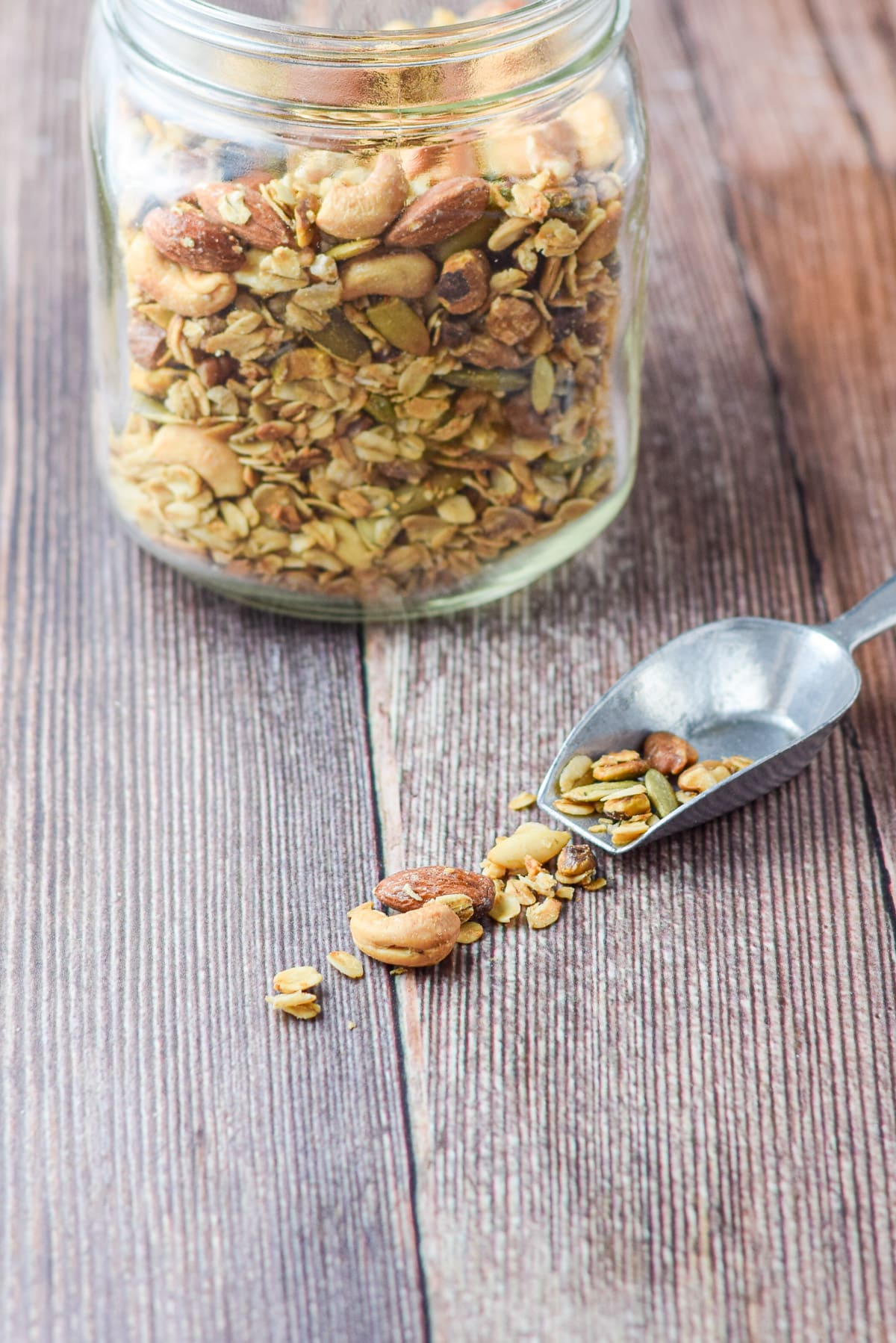 The scoop on the table spilling some granola on the table with the jar in the background