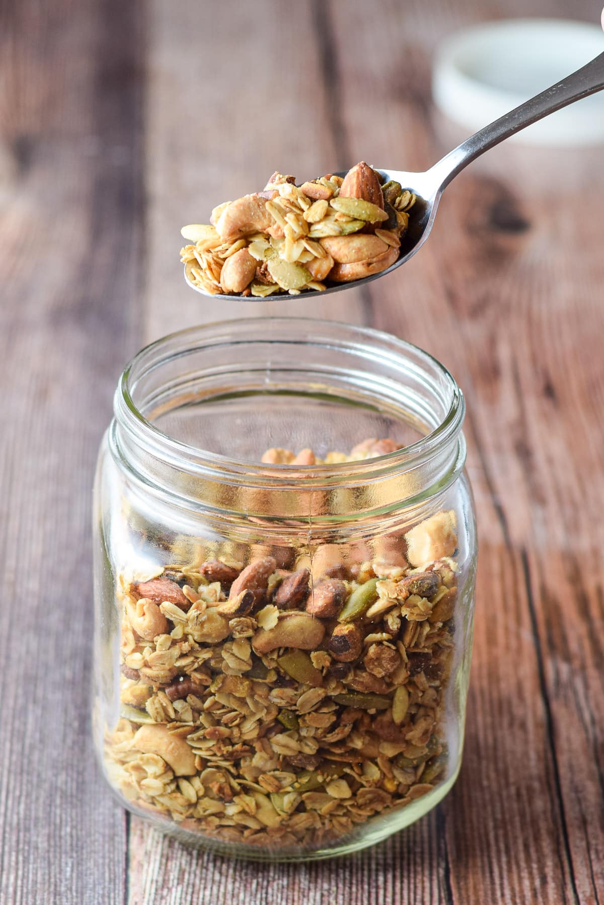 A hand holding a spoon of granola over the jar