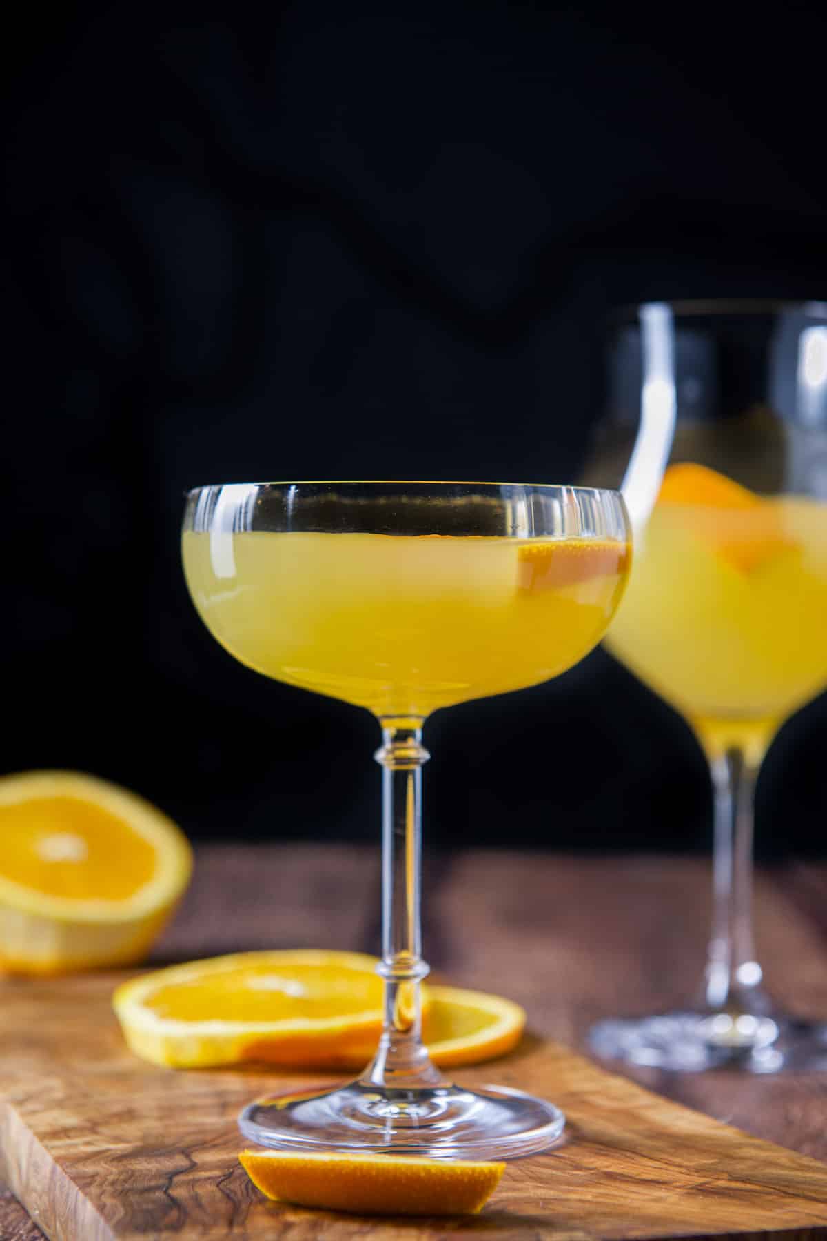 Vertical view of the two cocktail glasses filled with the drink with oranges on the board and table
