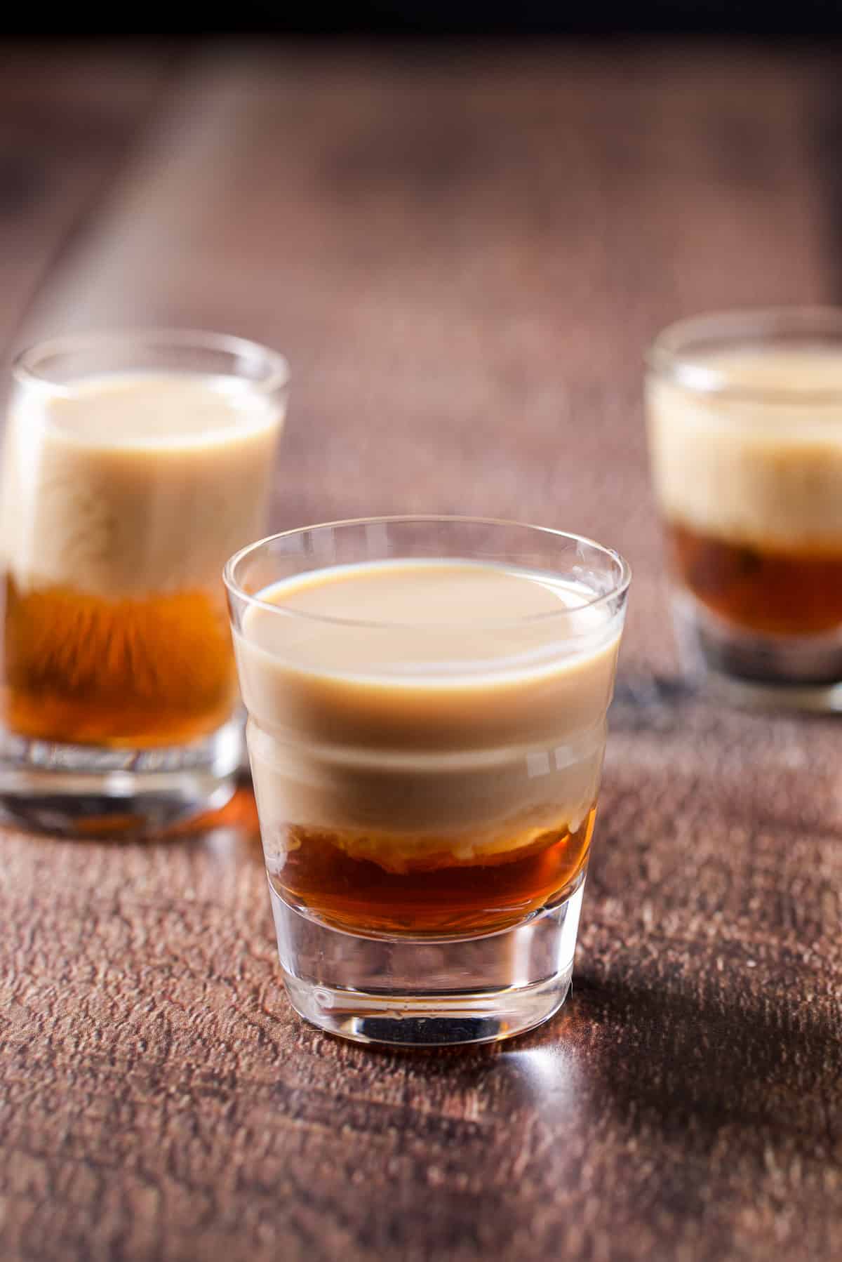 A beveled glass in front of the other glasses with the layered drink in it